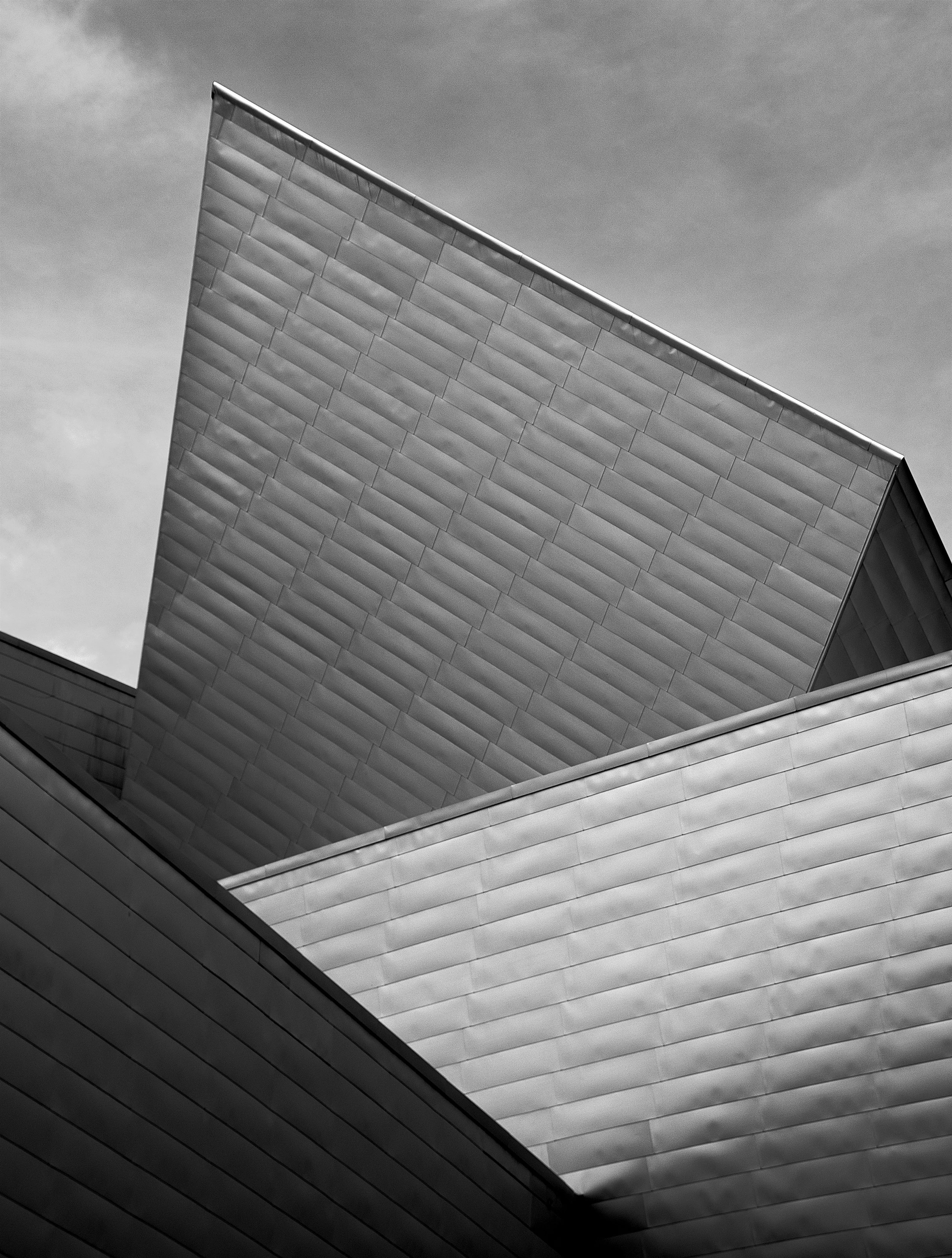 Close-up black and white photograph of a modern building with a geometric, angular design, showing multiple slanted and layered surfaces.