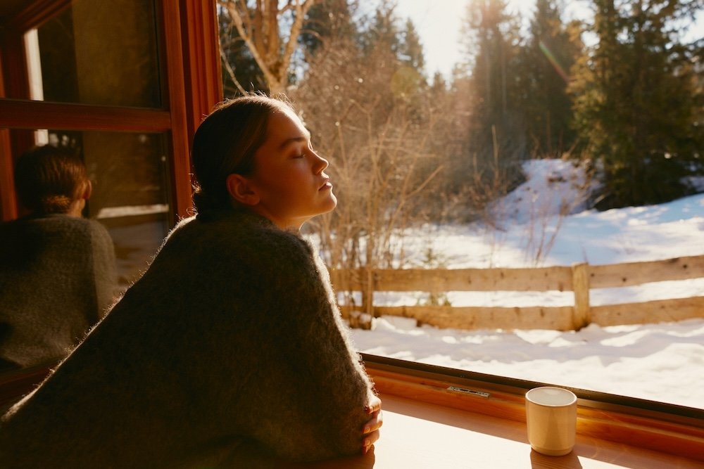 Woman looking out a window with natural light on her face.
