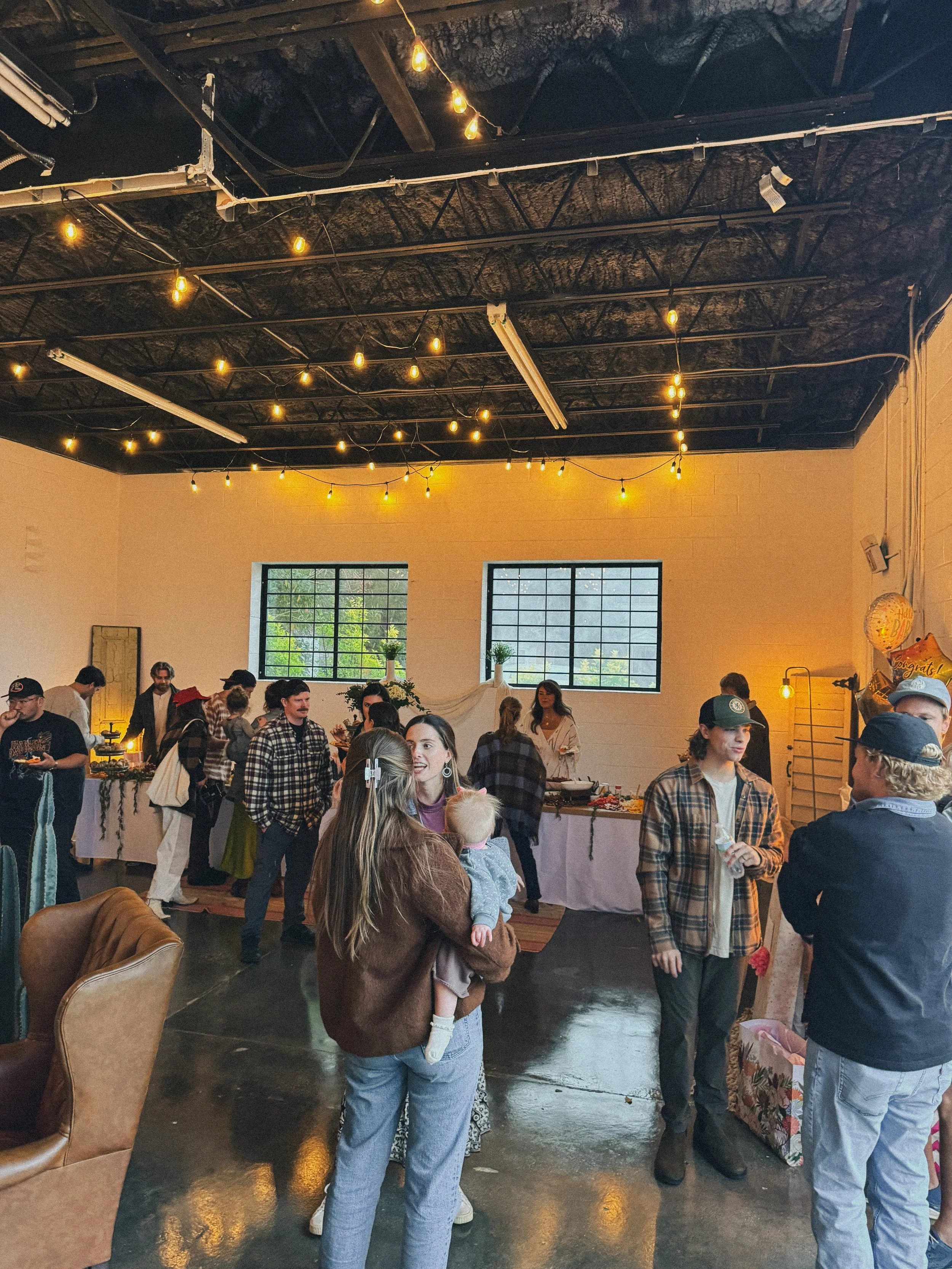 People socializing at an indoor event with string lights and food tables, some holding drinks.