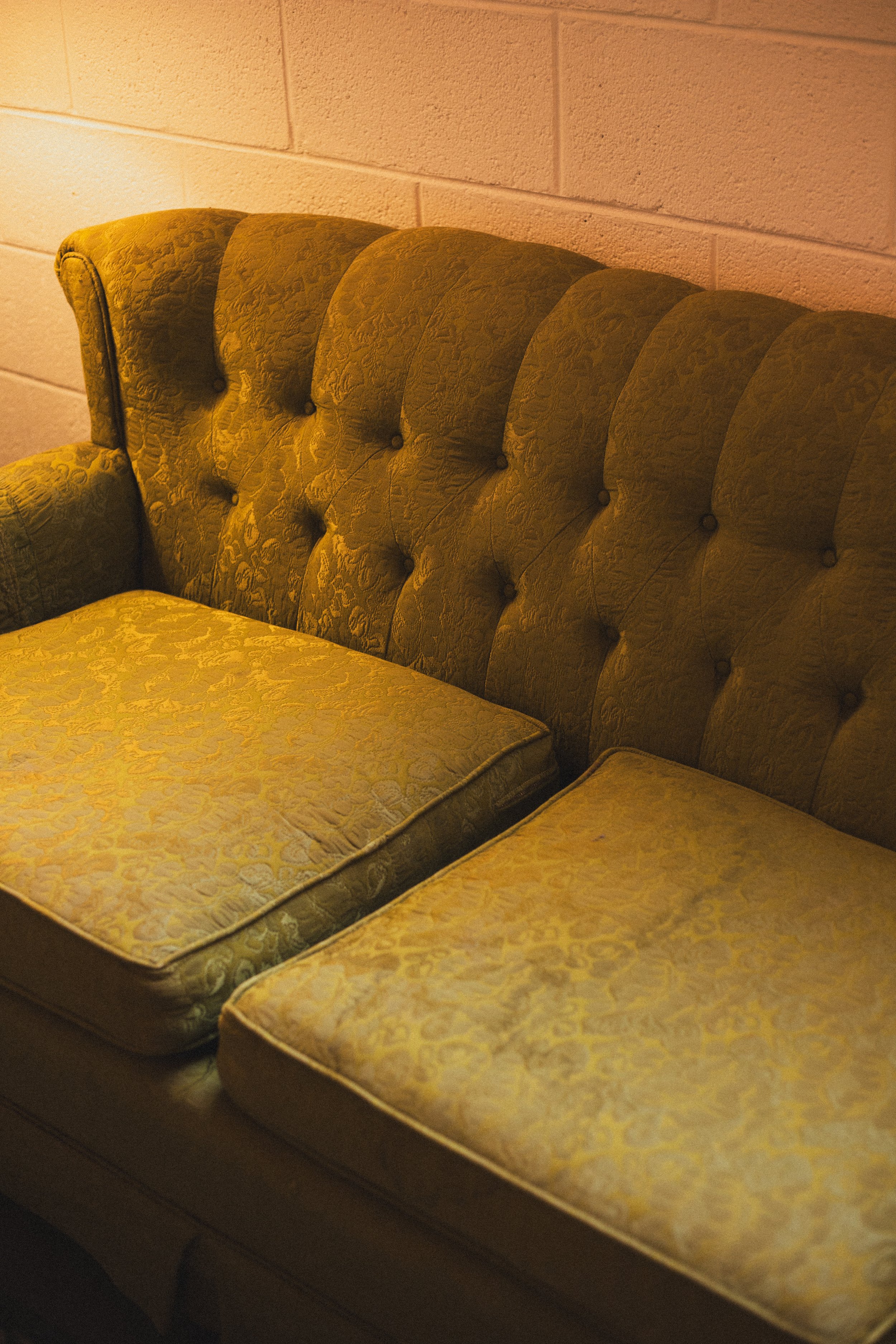 Four old, floral-patterned mattresses stacked together against a beige cinder block wall in a dimly lit room.