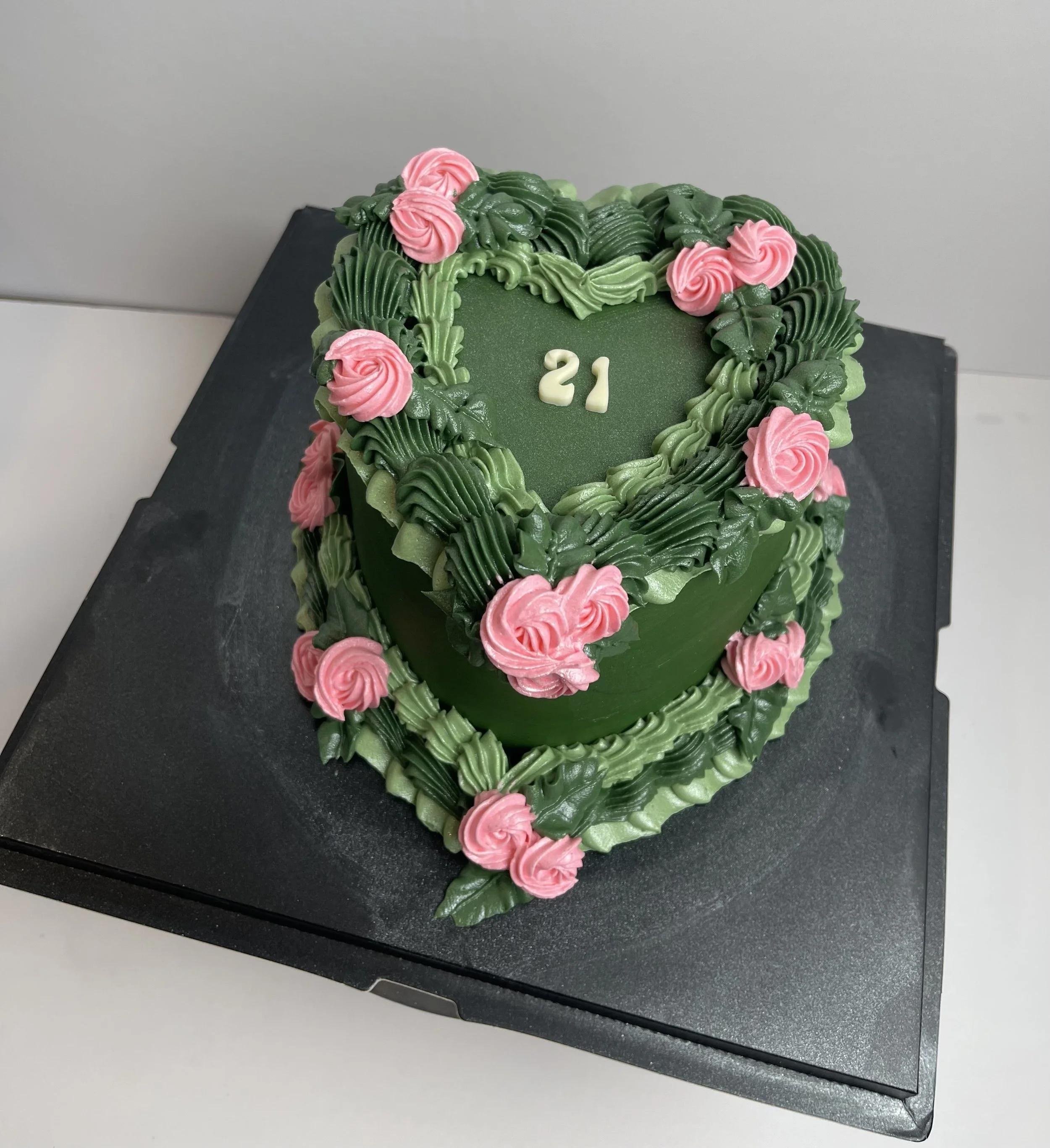 A green heart-shaped cake decorated with pink roses and green leafy icing, with the number 21 in white on top.