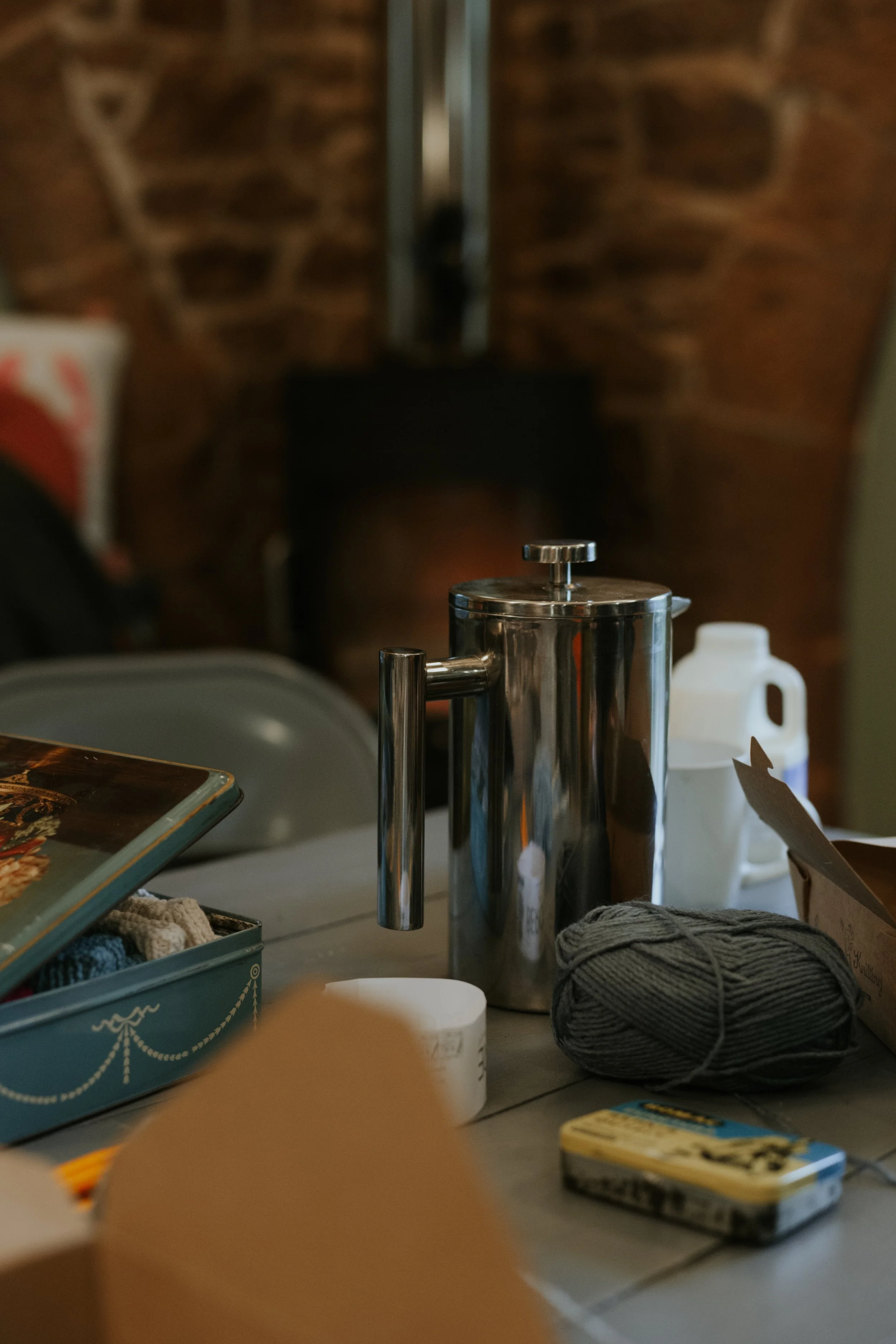 Cafetiere on table surrounded by knitting infront of a log burning stove