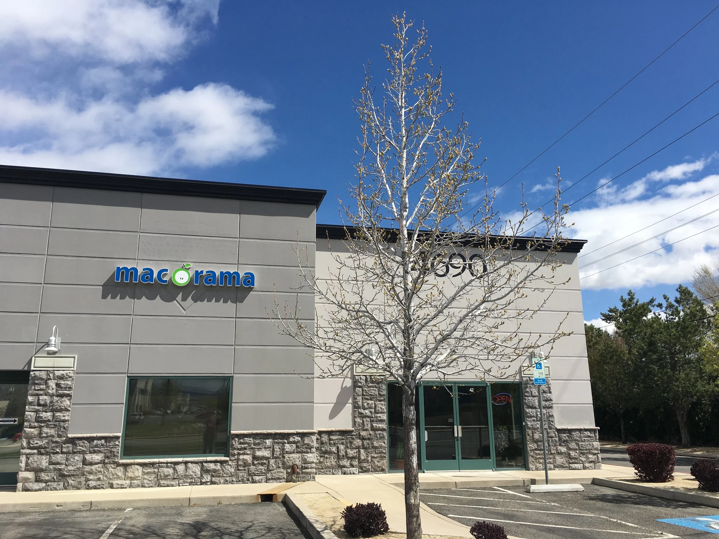 Exterior of a Macorama store with a leafless tree in front, parking lot, and blue sky with clouds.