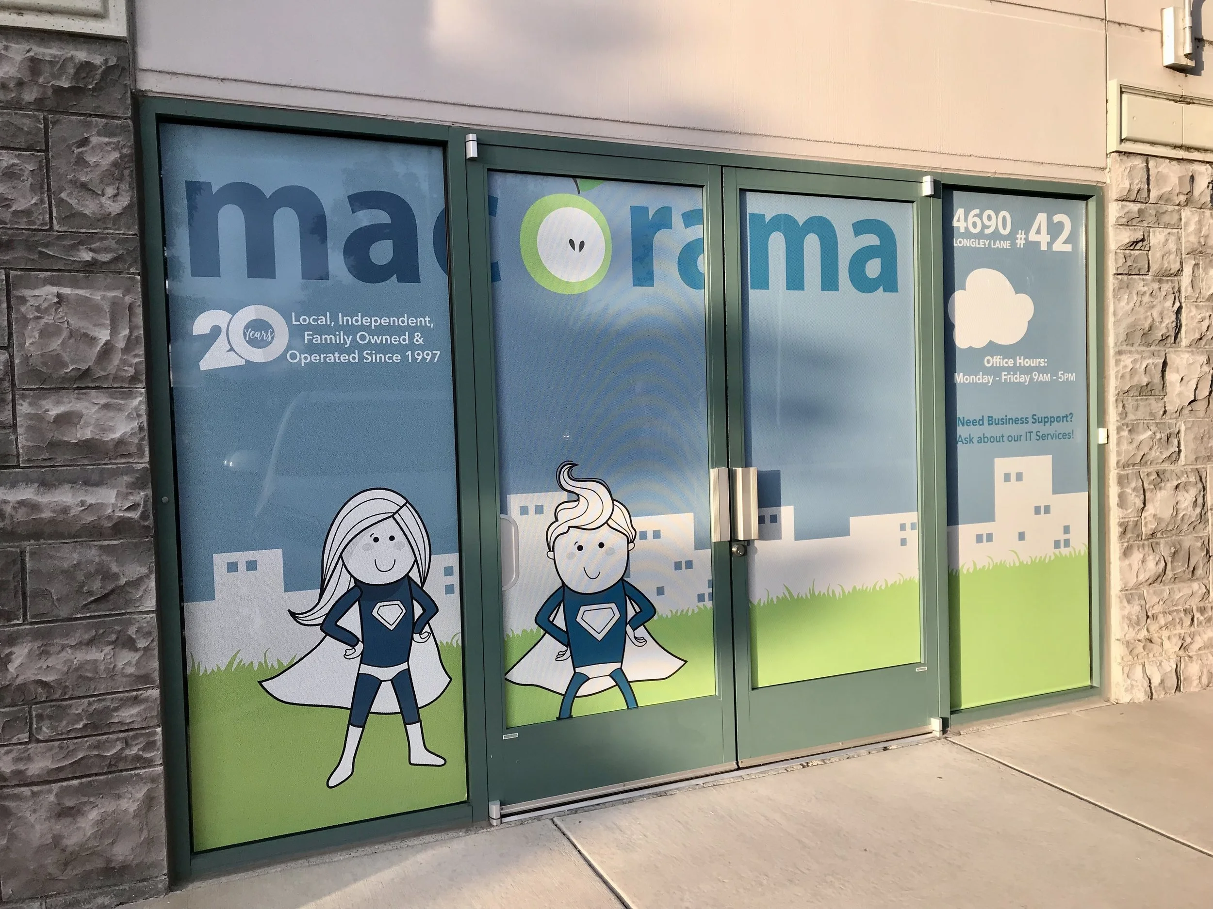 Storefront glass door with cartoon superhero characters, a girl with long hair and a boy with a swirl hairstyle, in front of a cityscape background with grassy area, with the store's name partially visible, logos, and office hours information.
