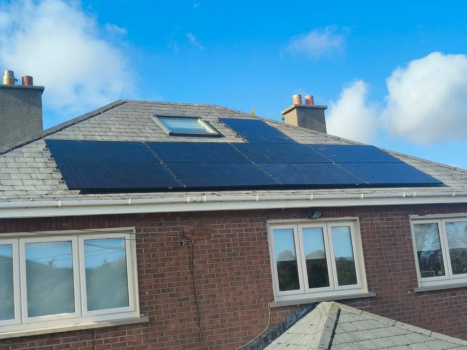 Residential house with solar panels installed on the roof near skylight, blue sky with some clouds in background.