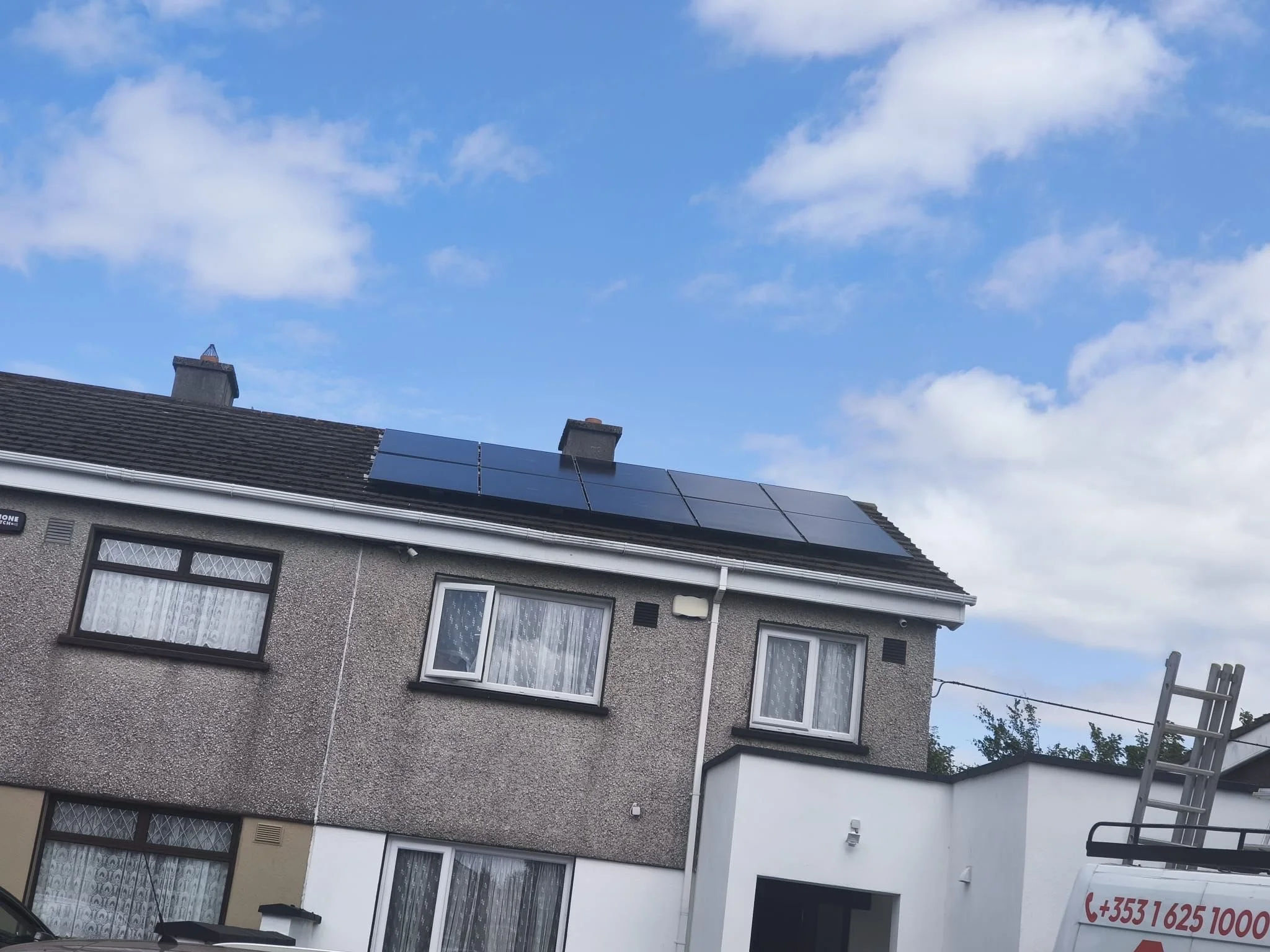 A house with solar panels installed on the roof, against a blue sky with scattered clouds.