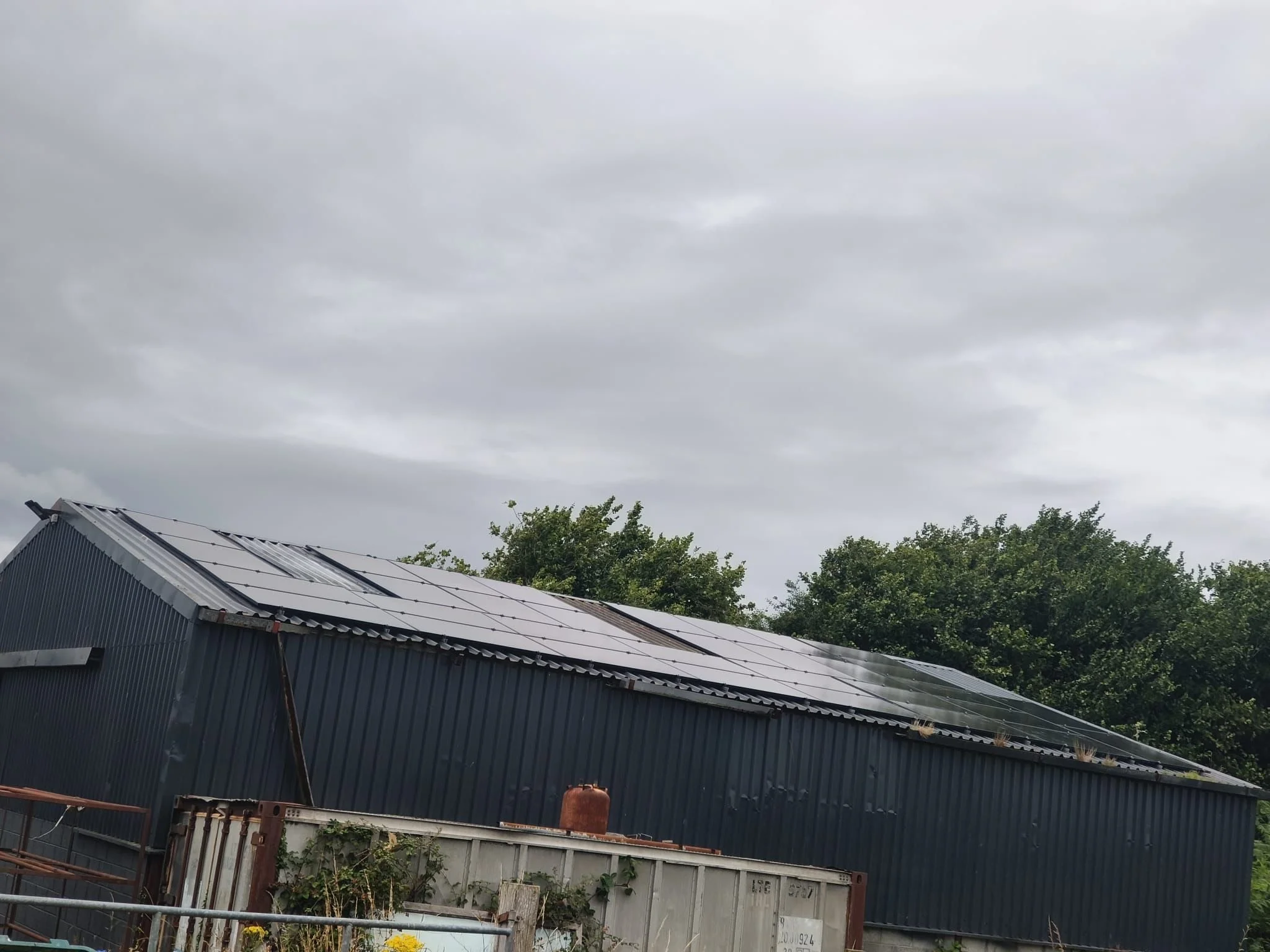 A metal building with solar panels installed on its roof under a cloudy sky.