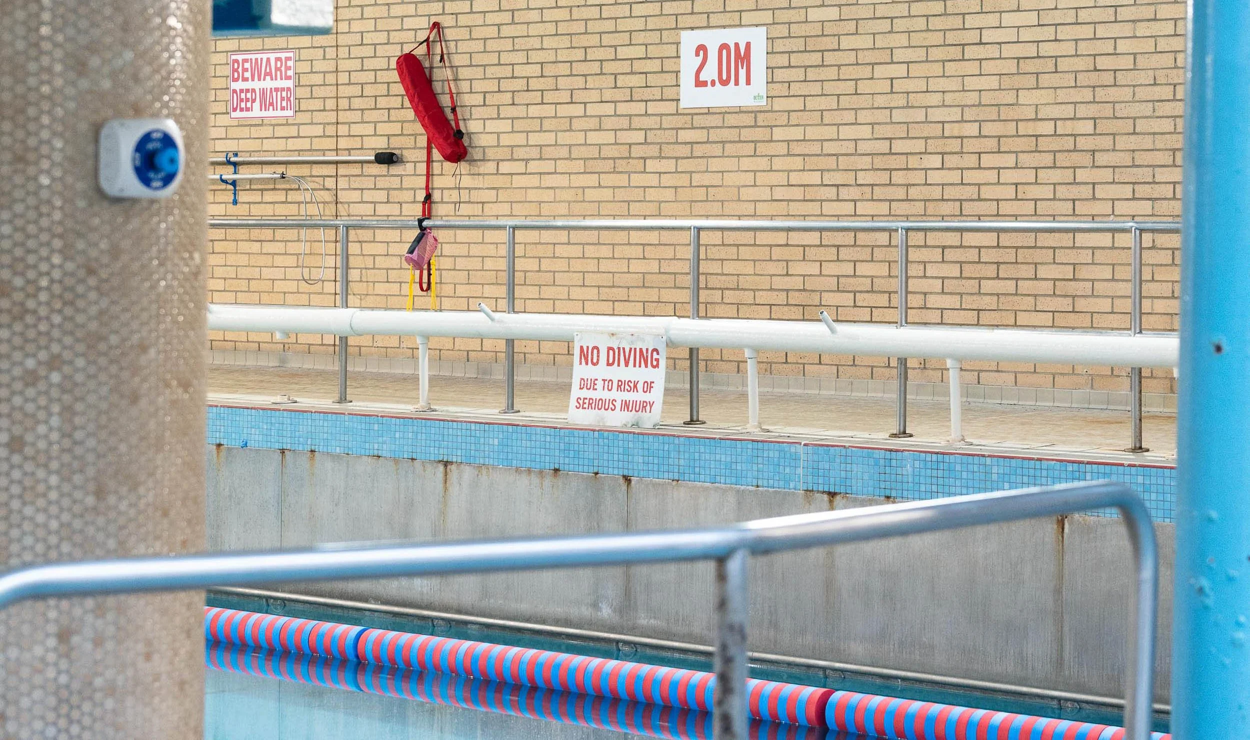 Public swimming pool area with caution signs, safety equipment, and drainage system. Waterfront Leisure Centre, Woolwich, London, England.