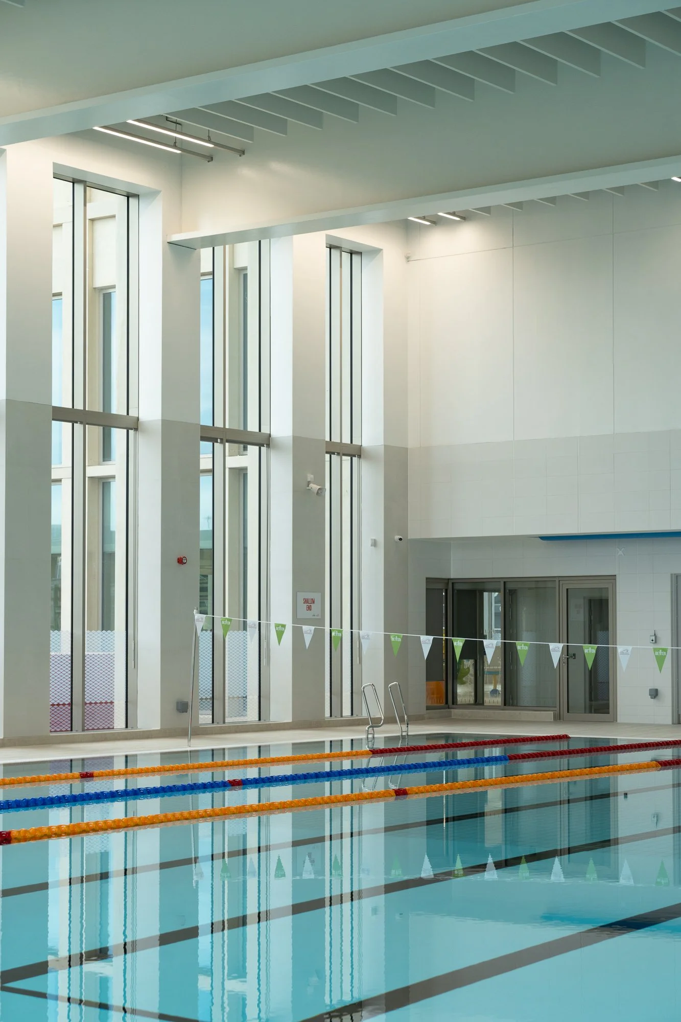 Indoor swimming pool with lane dividers, large windows, and high ceiling.