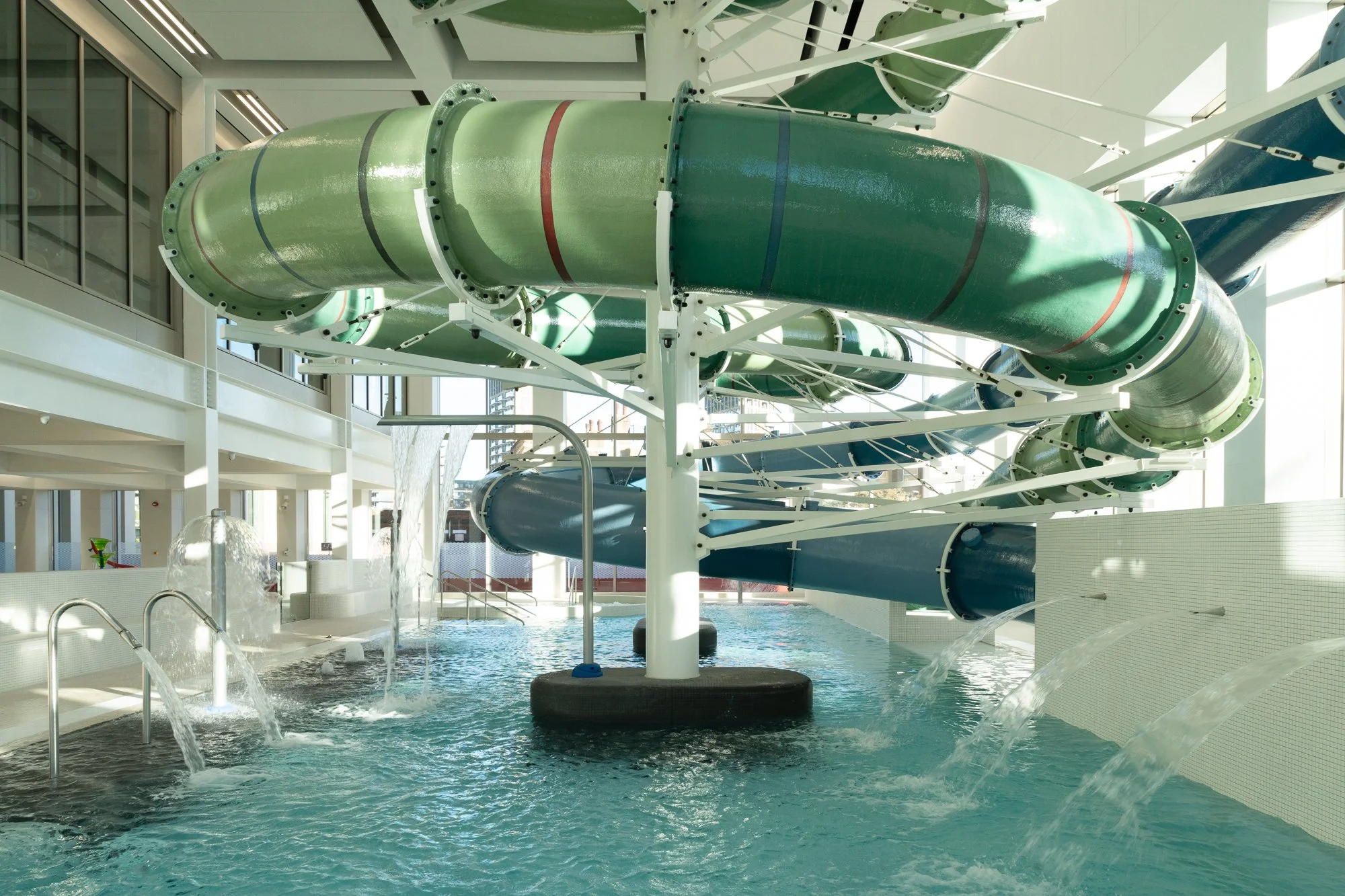 Indoor water park with large green and blue water slides over a shallow pool with fountains