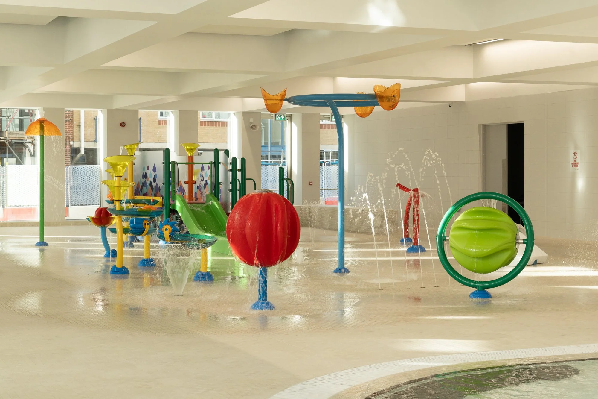 Indoor playground with colorful water fountains, slides, and play structures for children.