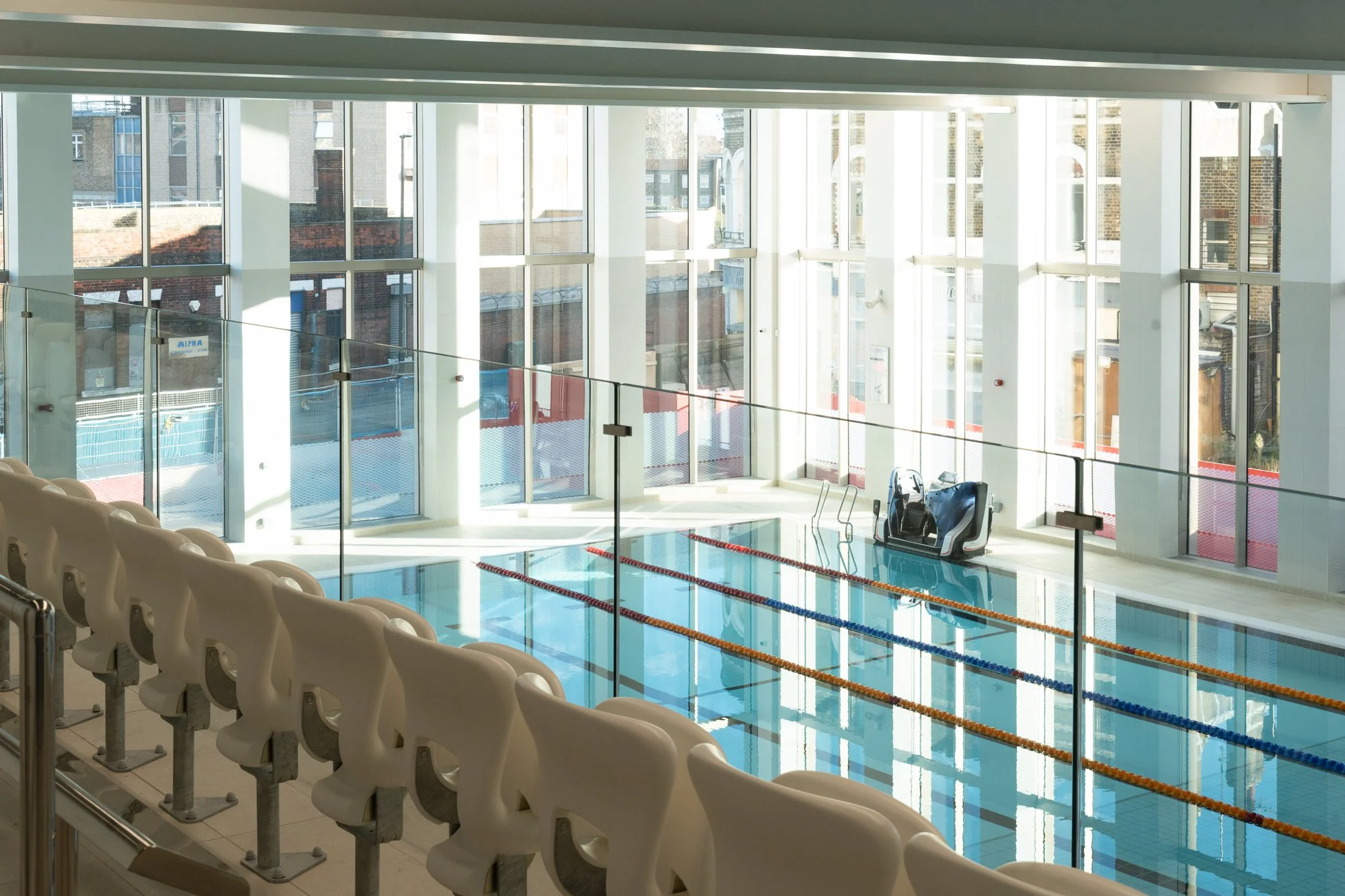 Indoor swimming pool with swimming lanes, white seating area, and large windows letting in natural light.