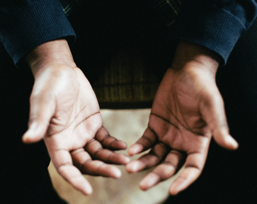 Person with hands open and palms up, wearing a dark long-sleeve shirt.