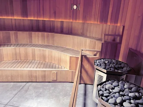 Indoor sauna with wooden benches and a heater filled with rocks.