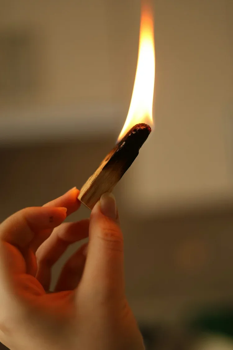 A hand holding a palo santo stick with a burning flame.