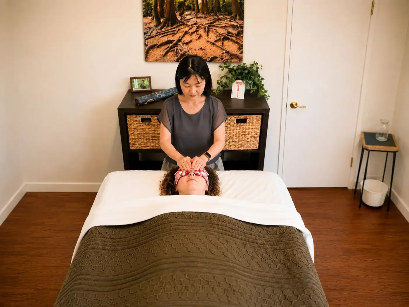 A female Reiki practitioner giving a treatment to a client lying face-up on a massage table in a cozy room.