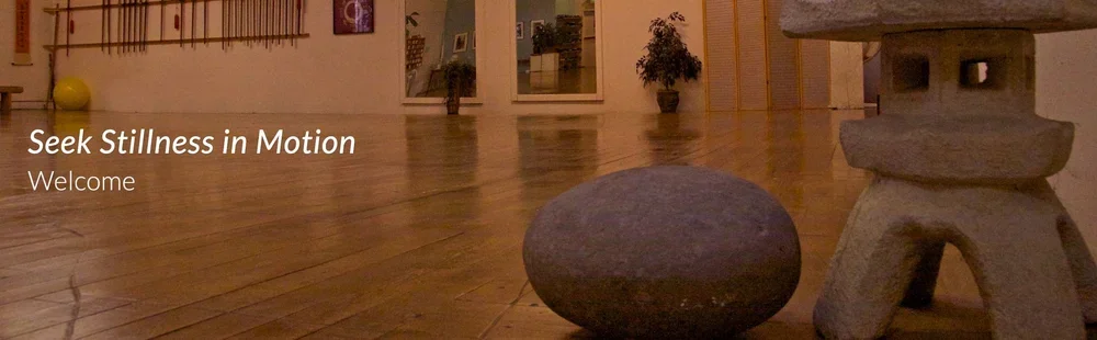 Indoor space with wooden flooring, stone sculpture, and potted plants in the background.