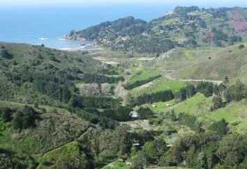Scenic view of rolling green hills and coastal landscape with ocean in the background.