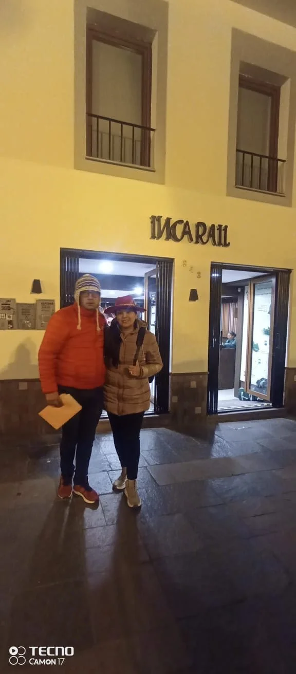 Dos personas de noche de pie frente a la entrada de un hotel llamado 'INCARAIL', vestidos con ropa de abrigo y sombreros, posando para la foto.