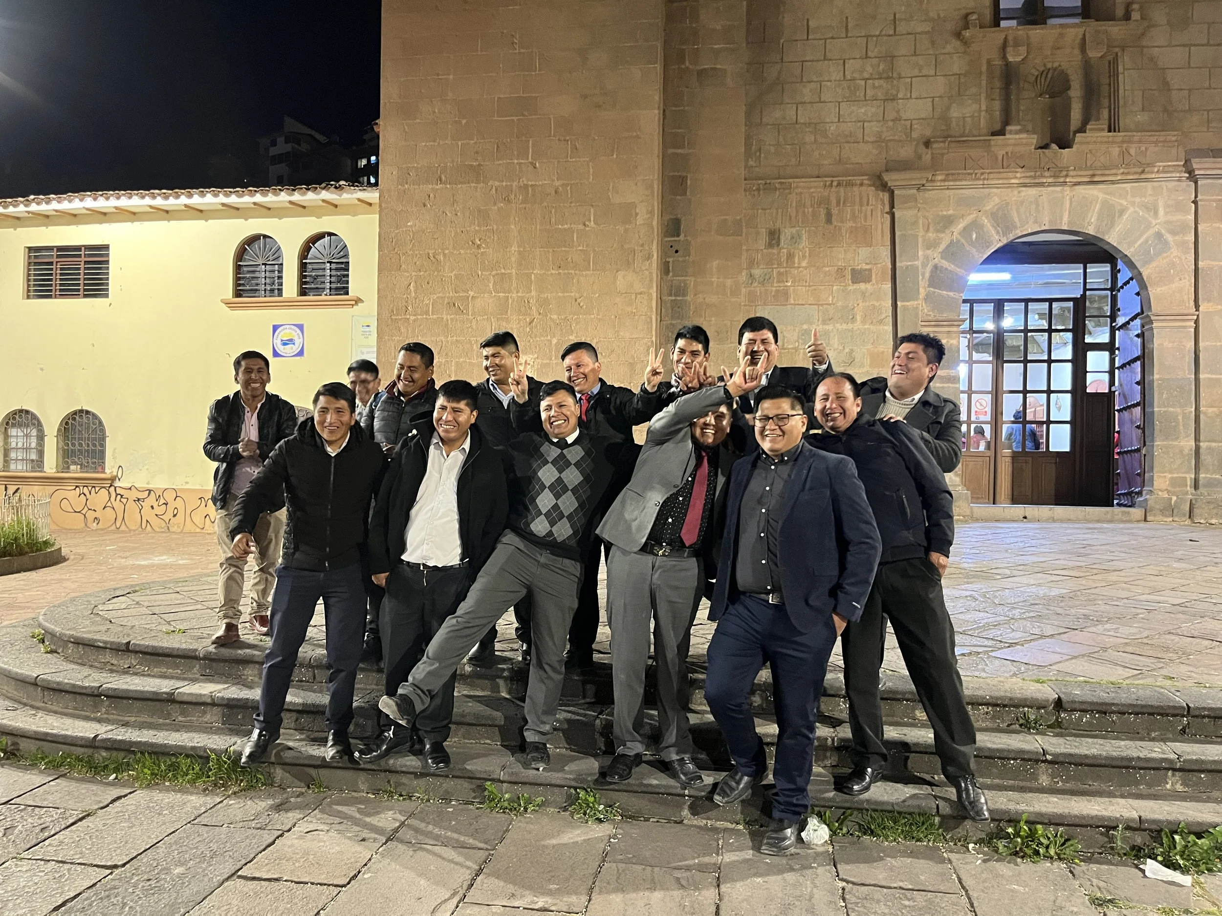 Grupo de hombres felices posando en las escaleras de una iglesia o edificio histórico de piedra, con risas y gestos felices, durante la noche.