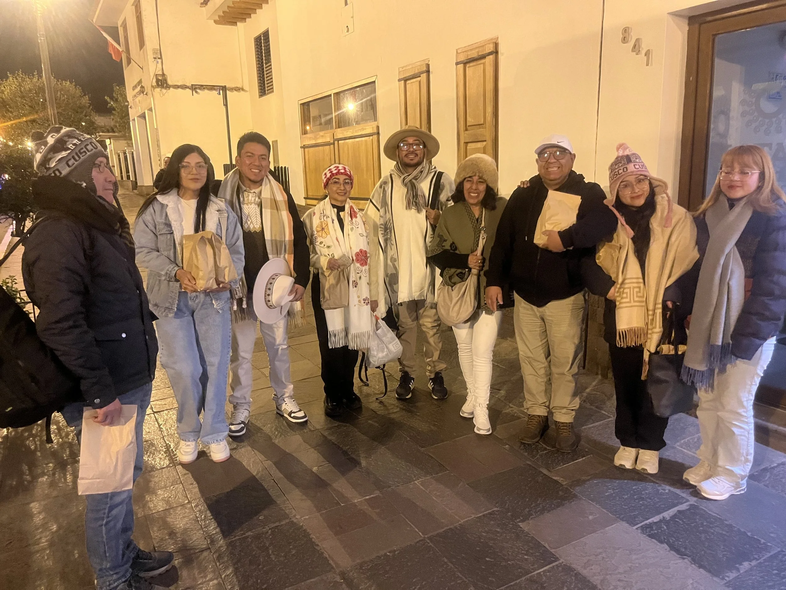 Grupo de personas posando en la calle en la noche, algunas llevan gorros y bufandas.