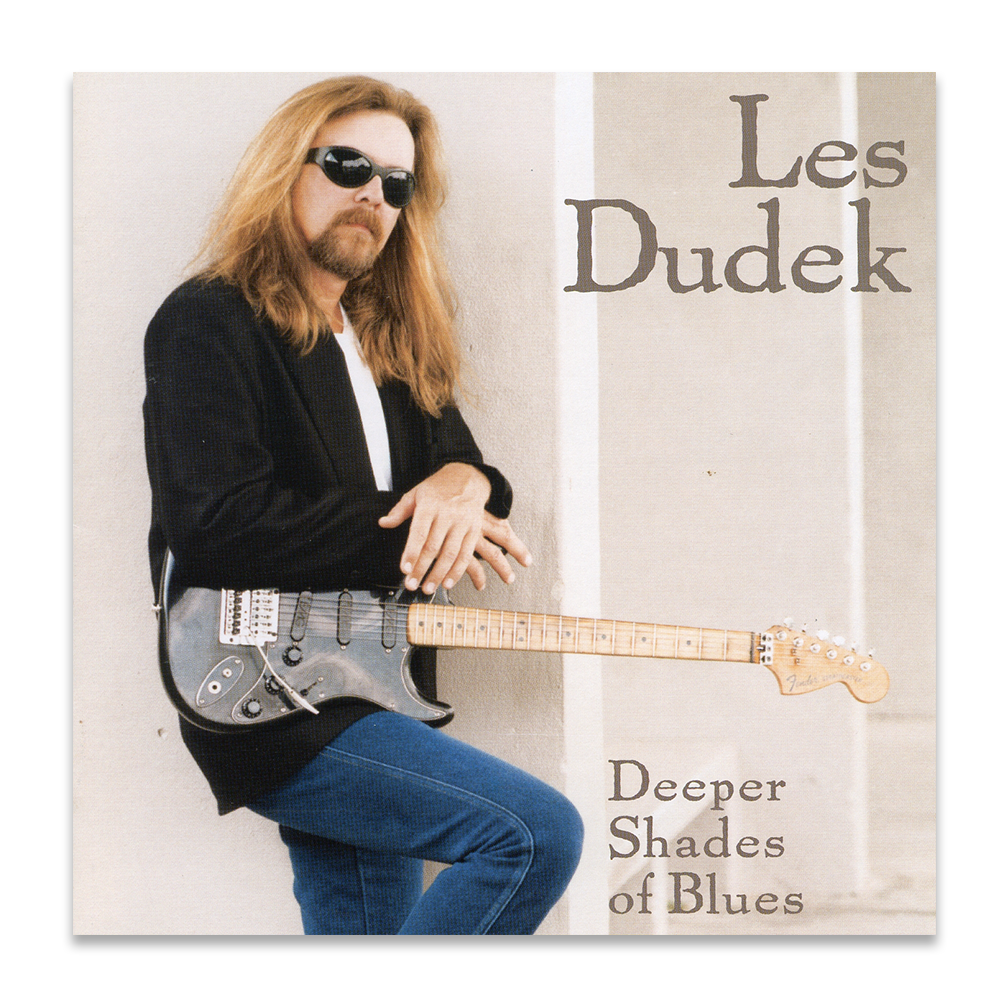 Album cover of Les Dudek sitting with sunglasses, holding a guitar, wearing a black jacket and blue jeans, with the title "Deeper Shades of Blues" visible.
