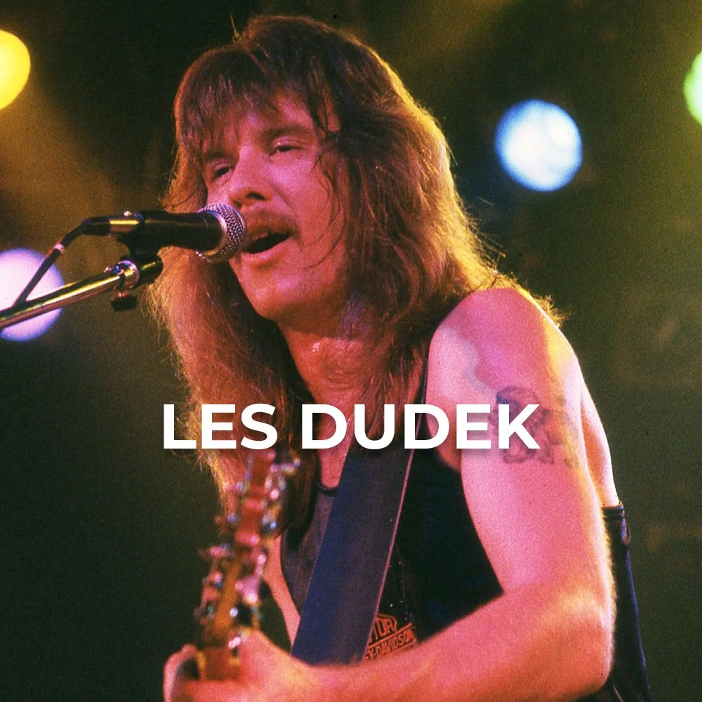 A long-haired musician singing into a microphone with a guitar, in a performance setting with colorful stage lights, text overlay reading 'Les Dudek'.