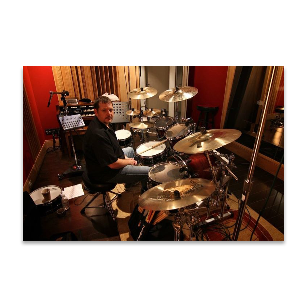 Man sitting at a drum set in a recording studio.