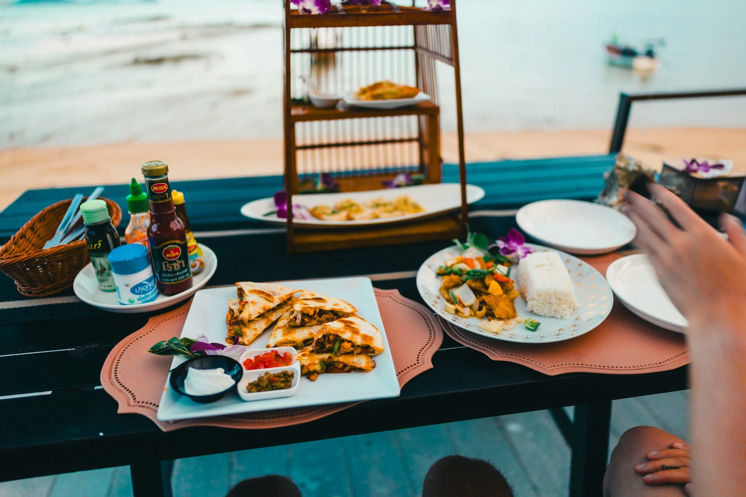 Seaside table set with vibrant dishes and sauces near sparkling water, capturing the flavor and beauty of global travel with Legacy Reserve Travel.
