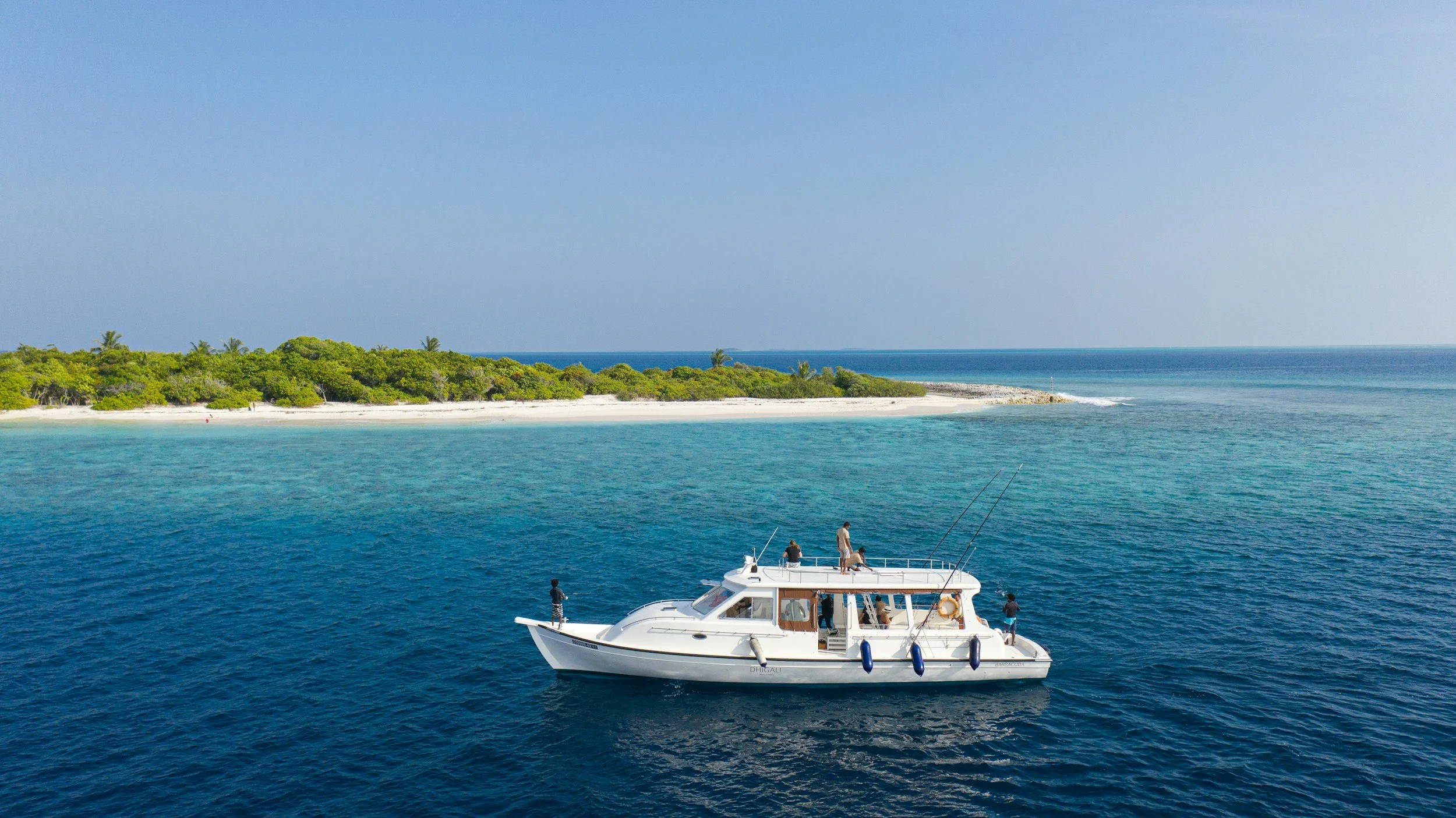 Luxury yacht with travelers fishing in clear blue waters near a tropical island, part of a Legacy Reserve Travel ocean getaway.