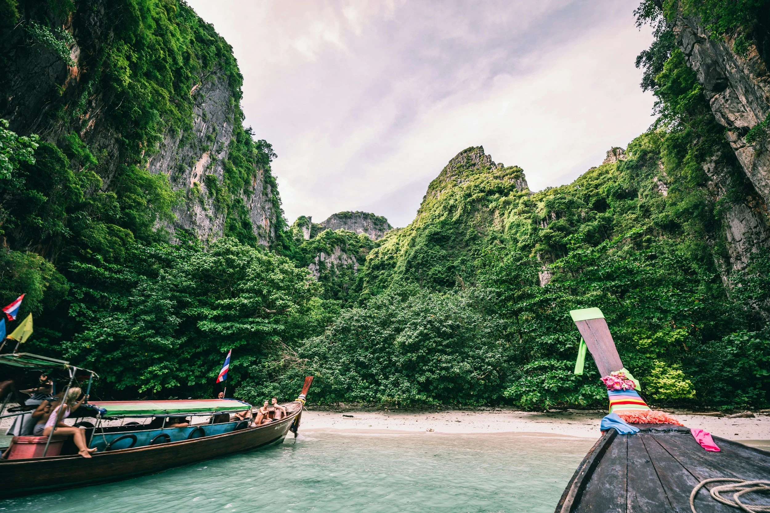 Scenic view of lush jungle cliffs and sandy beach from a boat on turquoise water, capturing a tropical Thailand adventure with Legacy Reserve Travel.