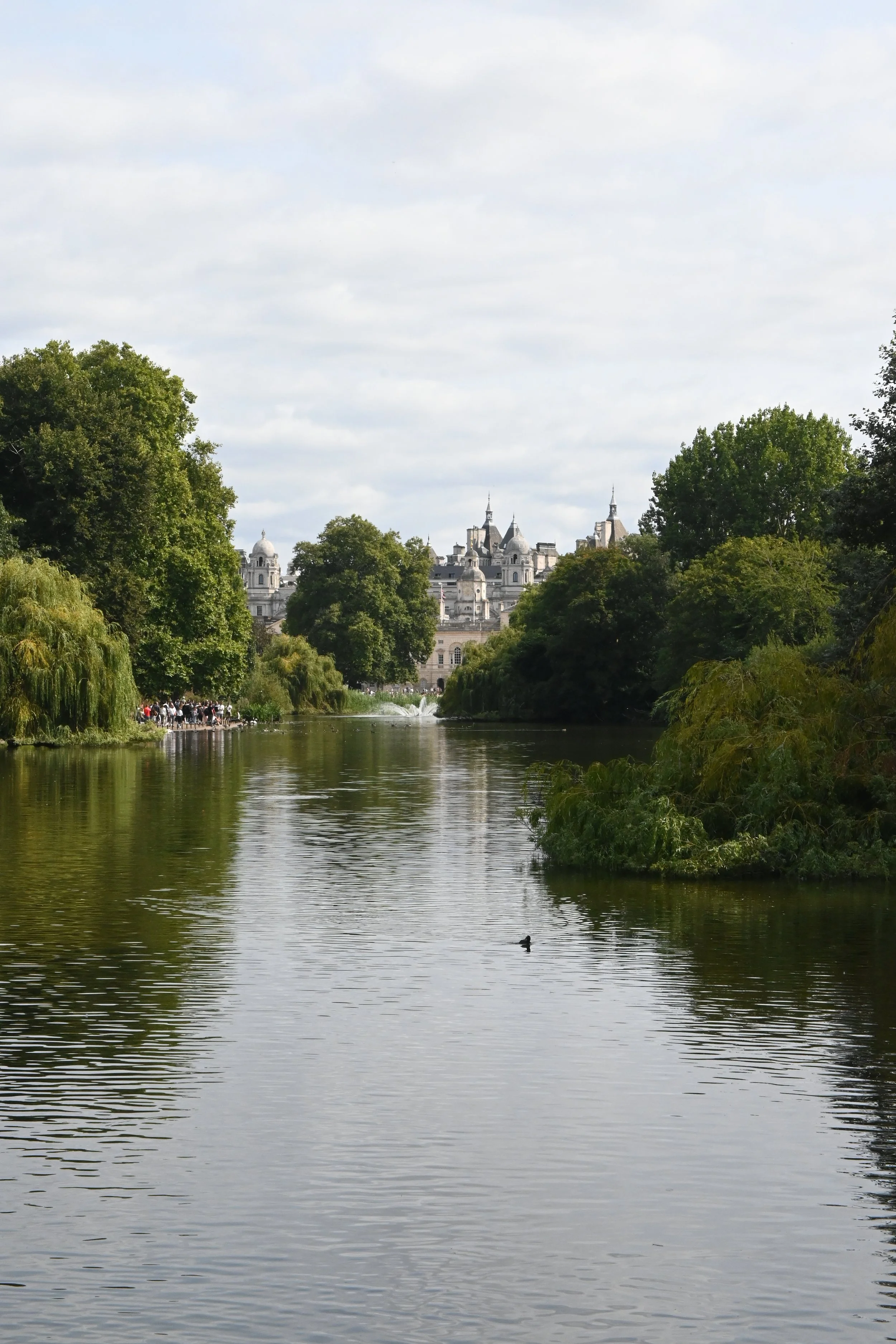 Un fiume circondato da alberi verdi con un castello in stile gotico sullo sfondo sotto un cielo parzialmente nuvoloso. Regent's Park a Londra.
