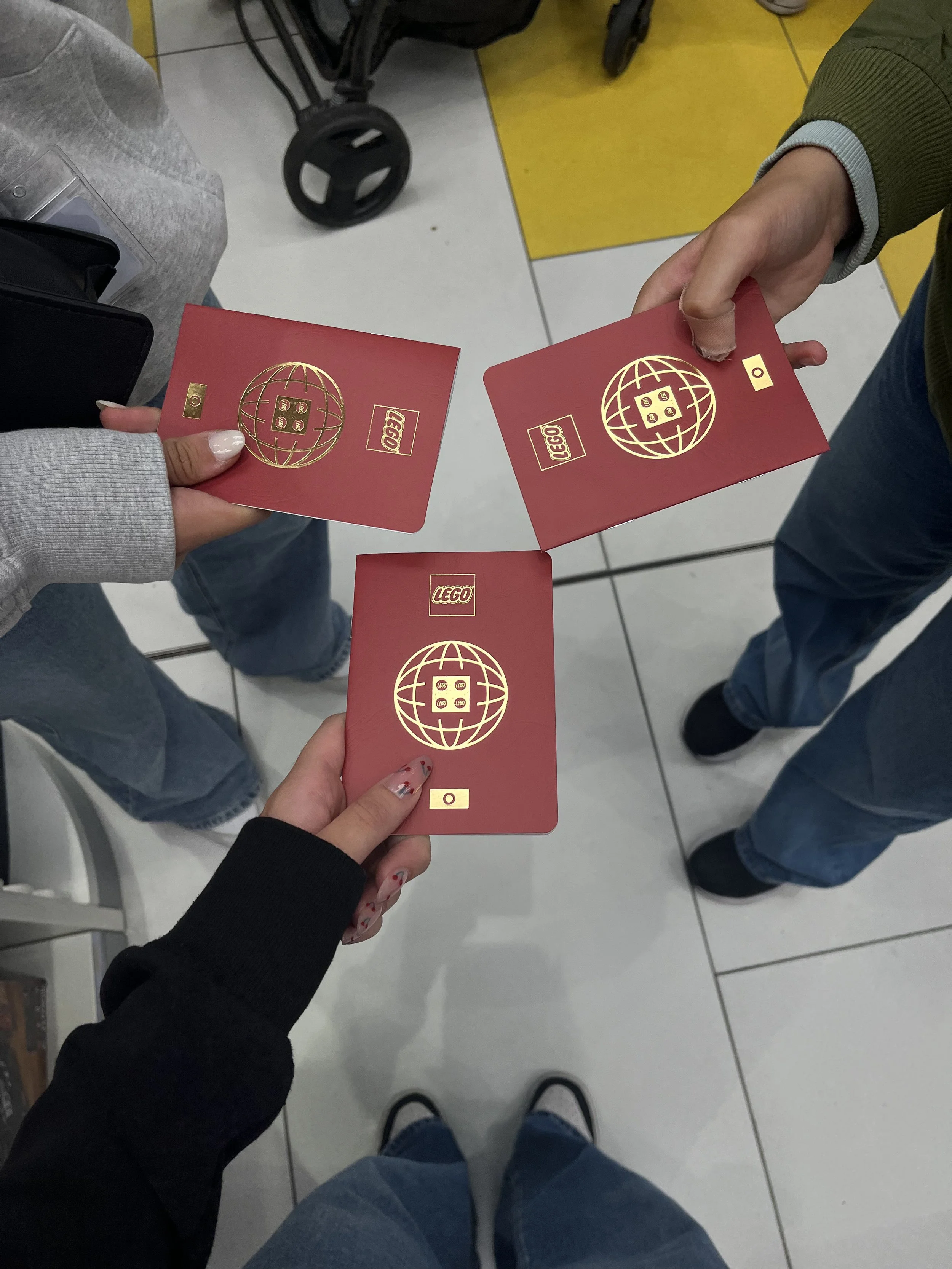 Tre persone tengono in mano delle carte rosse con il logo LEGO e un disegno di un globo terrestre dorato, probabilmente cartoline o biglietti.