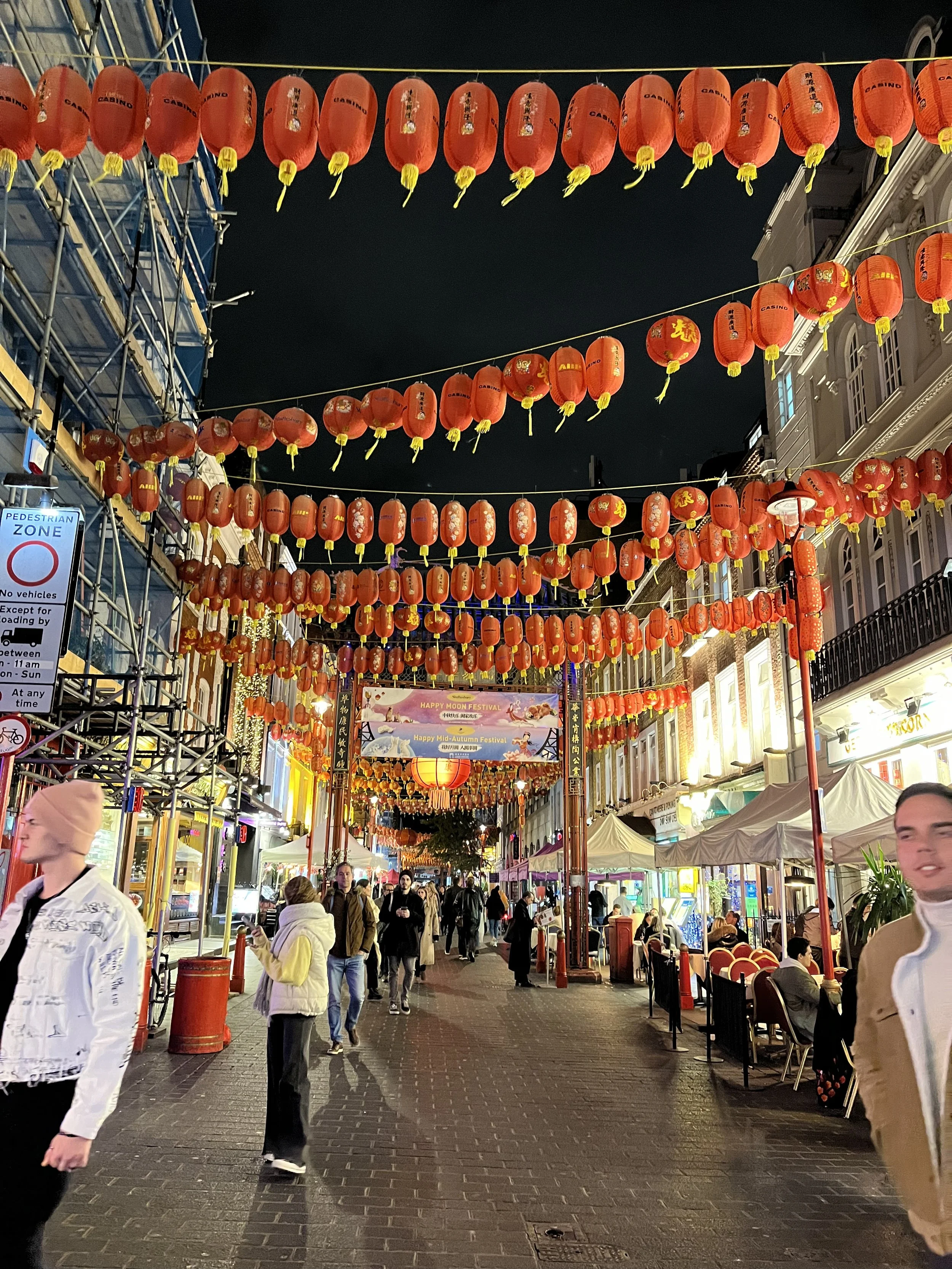 Strada affollata decorata con lanterne rosse luminose e bancarelle con cene all'aperto durante una festa cinese o asiatica notturna.