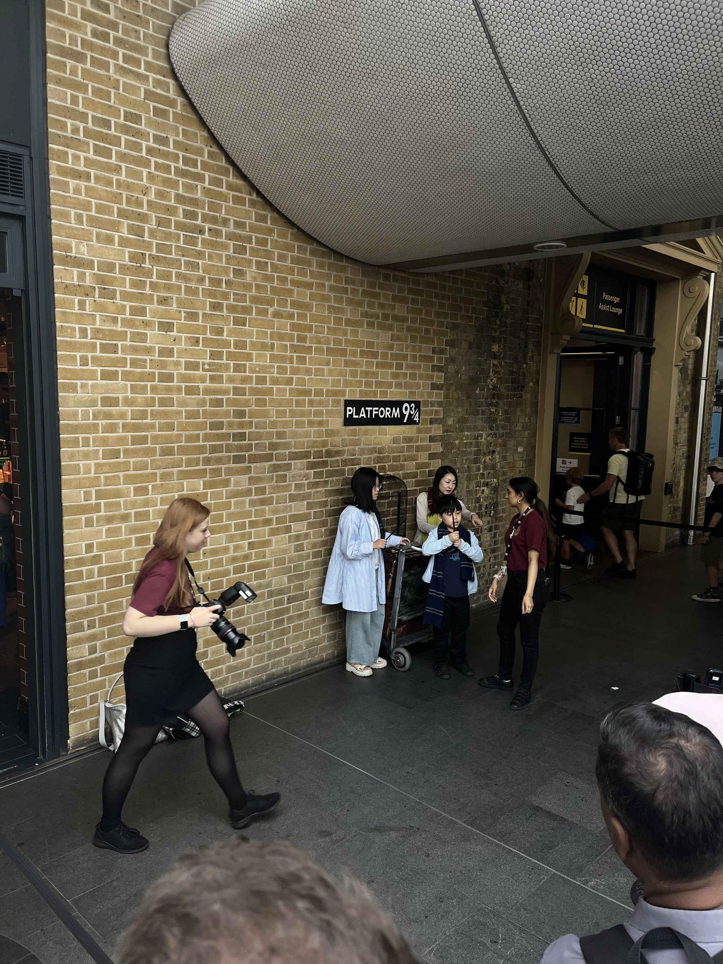 Gruppo di persone davanti all'ingresso di una stazione, con un cartellino 'Platform 9¾'. Piattaforma di Harry Potter.