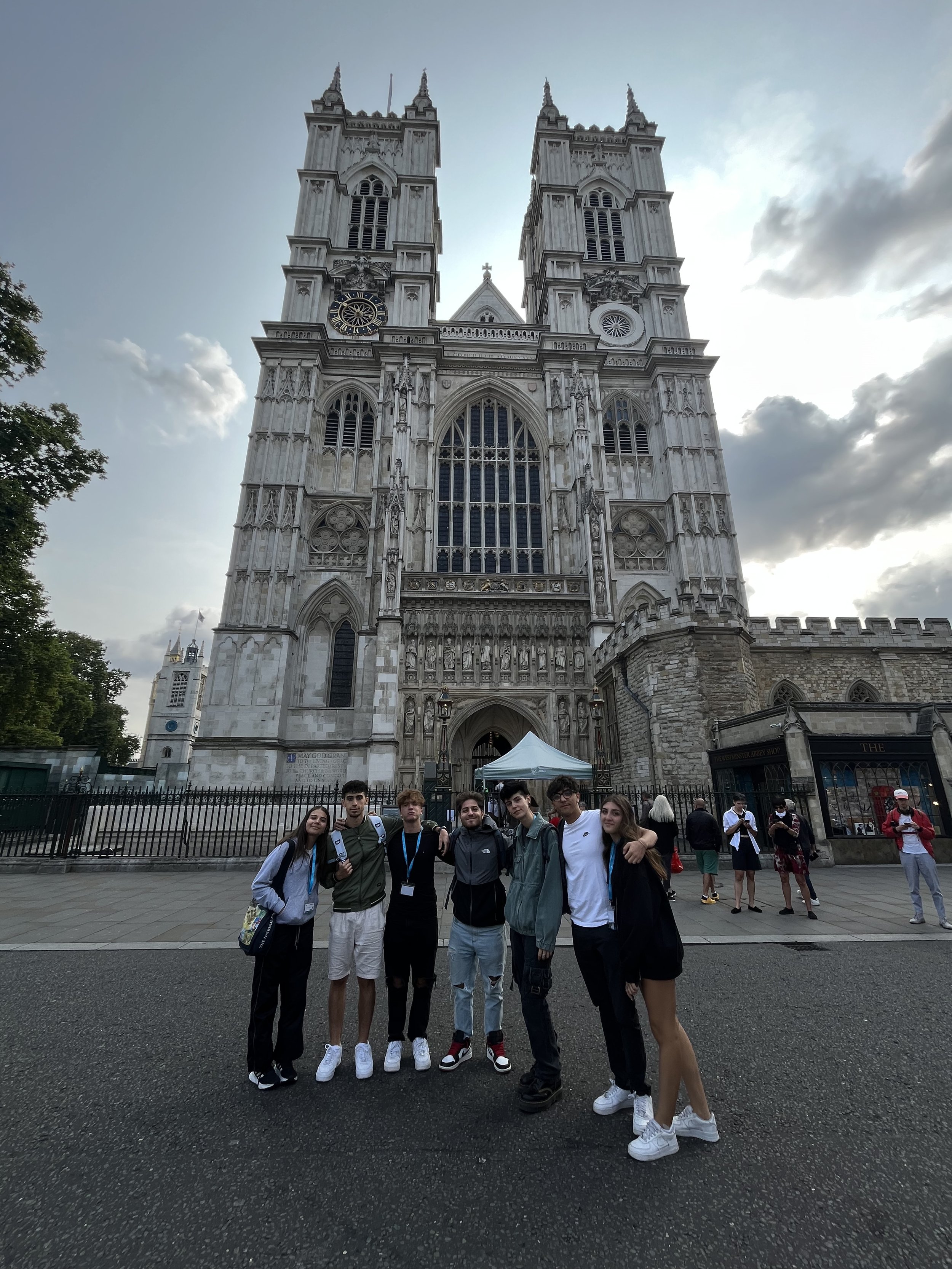 Gruppo di giovani davanti a Westminster Abbey a Londra, con la chiesa gotica sullo sfondo e un cielo parzialmente nuvoloso.