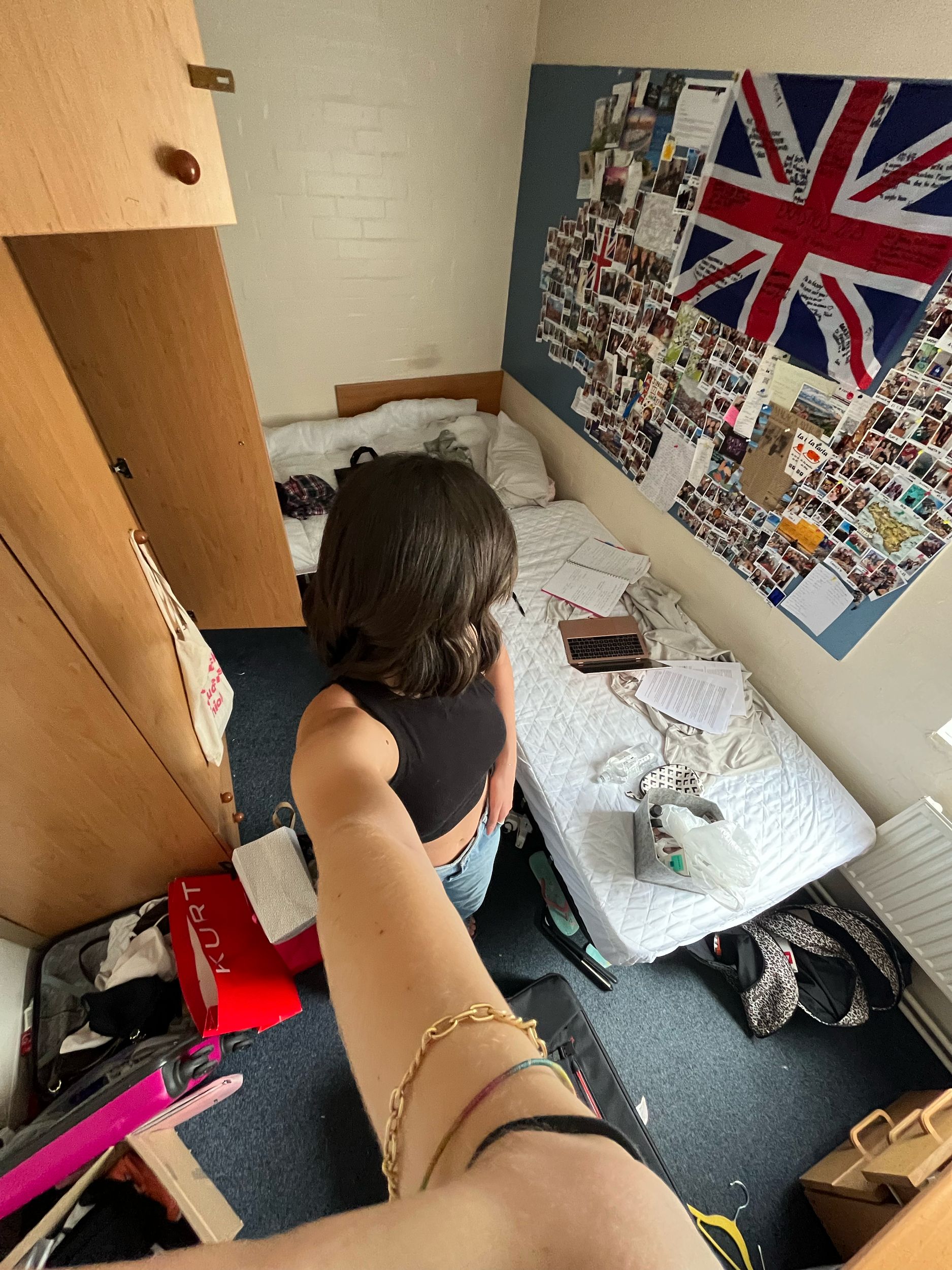 Stanza di una camera da letto con parete decorata con una bandiera del Regno Unito e molte foto. Sul letto ci sono un laptop aperto, alcuni fogli e un sacchetto di plastica. Erasmus in Inghilterra, Università di warwick.