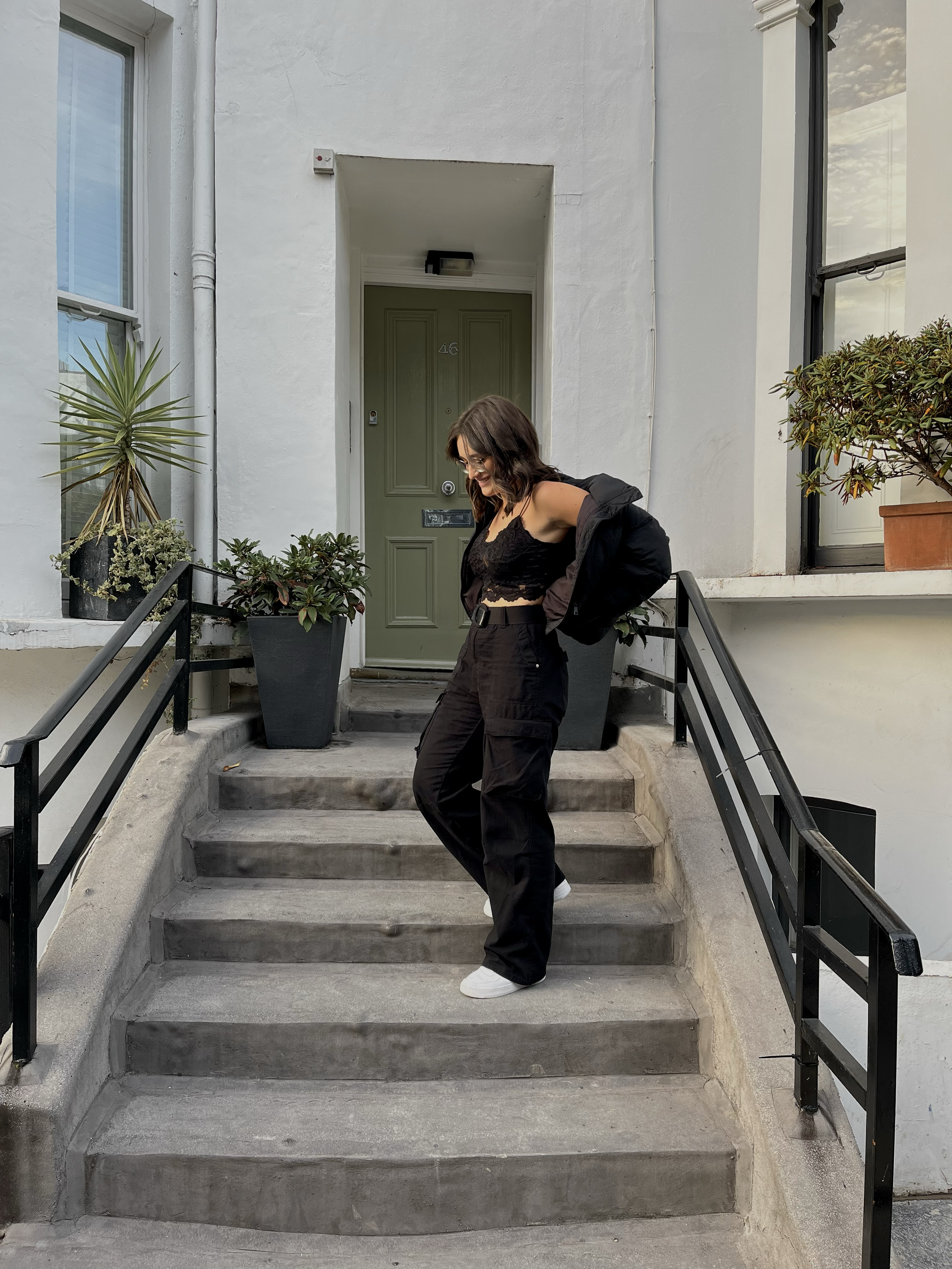 Una ragazza vestita di nero scende le scale di un edificio con una porta verde, piante in vasi neri ai lati. Ci troviamo a Notting Hill a Londra