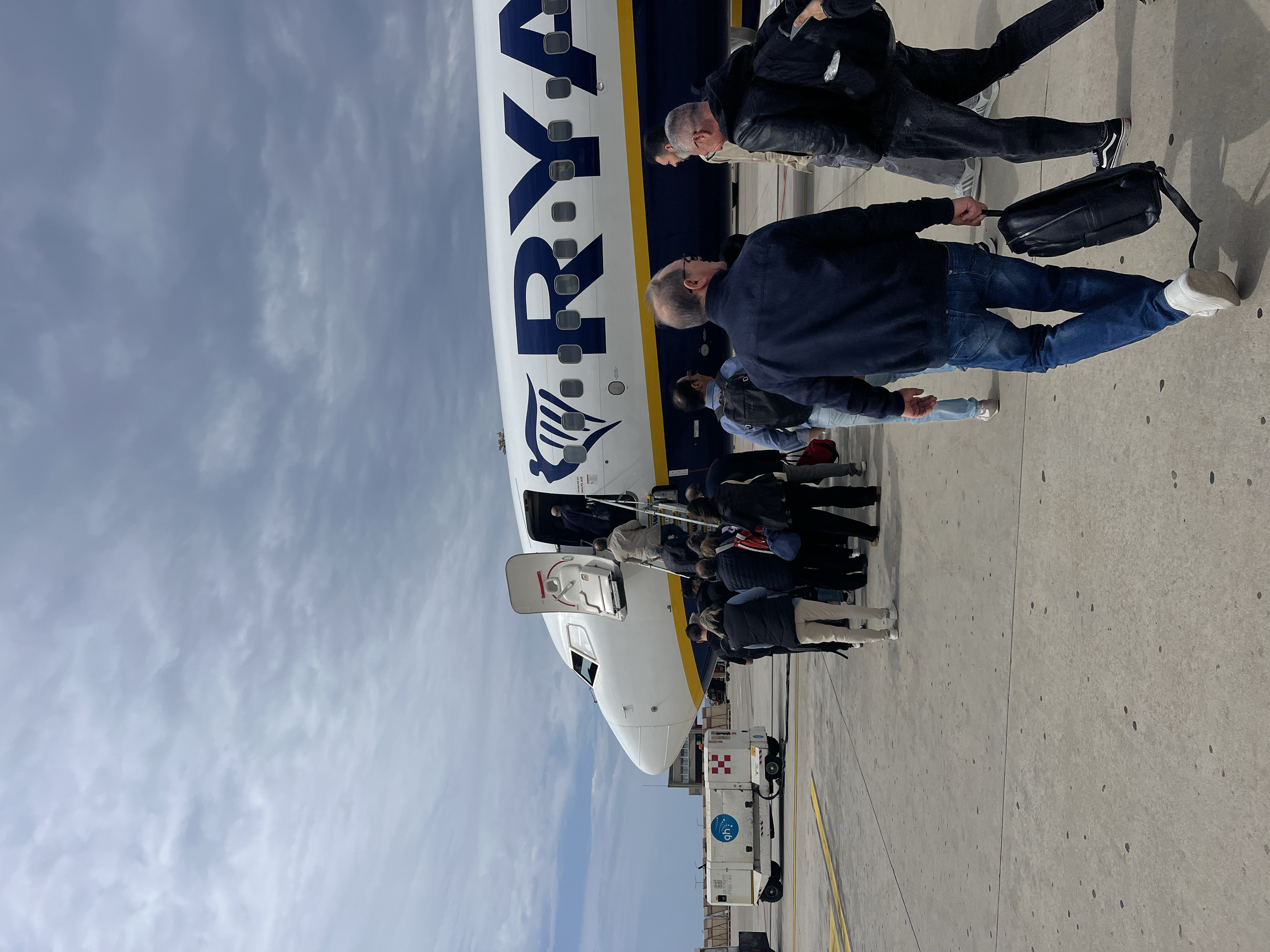Gruppo di persone che attendono di imbarcarsi su un aereo Ryanair in aeroporto, con alcuni che salgono gli scalini.
