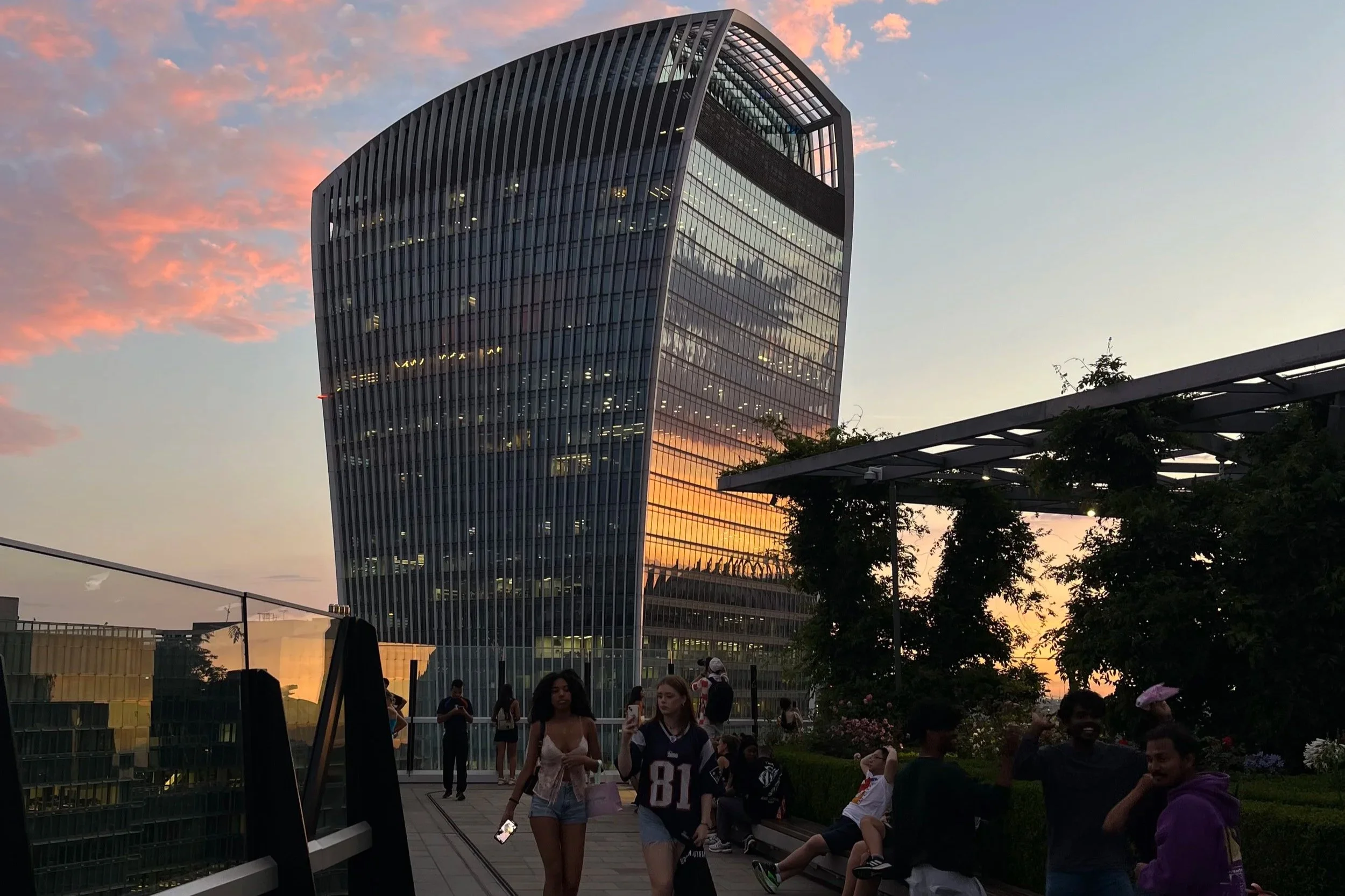 Un edificio moderno con facciate in vetro, al tramonto, con molte persone che camminano e si rilassano in un'area all'aperto sul tetto di un edificio
