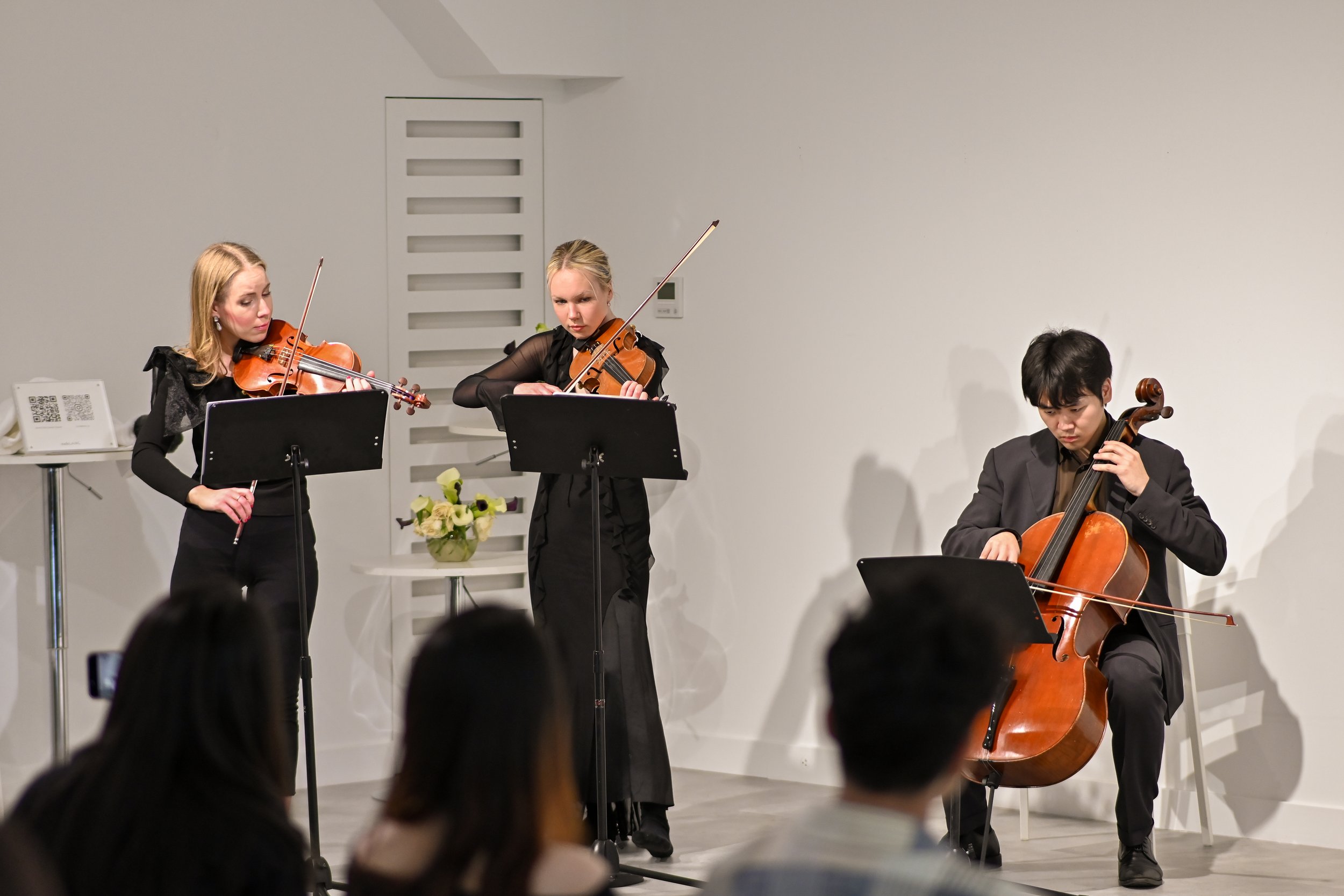 Two women playing violins and a man playing cello performing on stage during a concert.