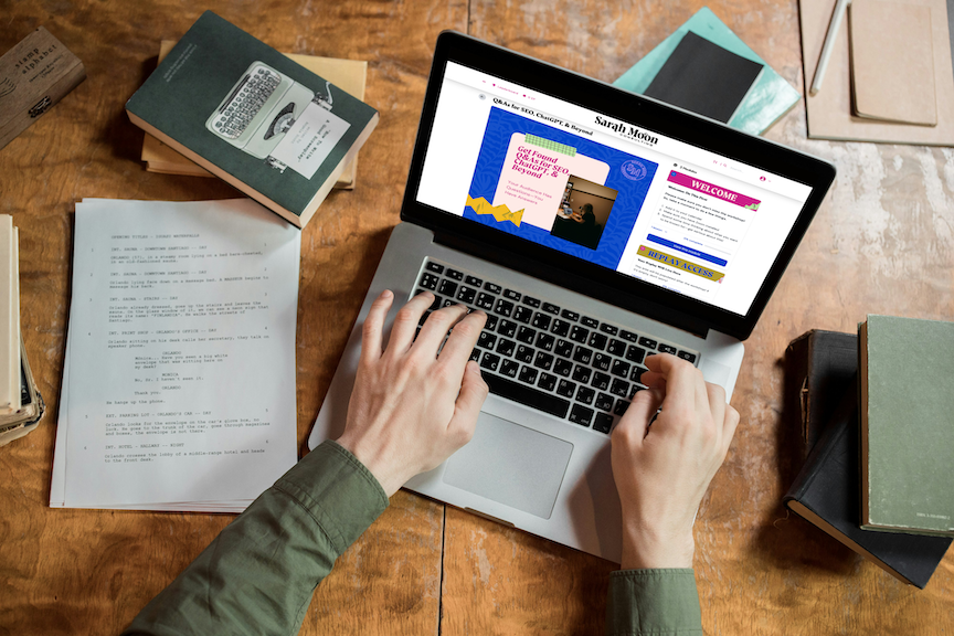 Person working on a laptop at a wooden desk with books, papers, and notebooks.