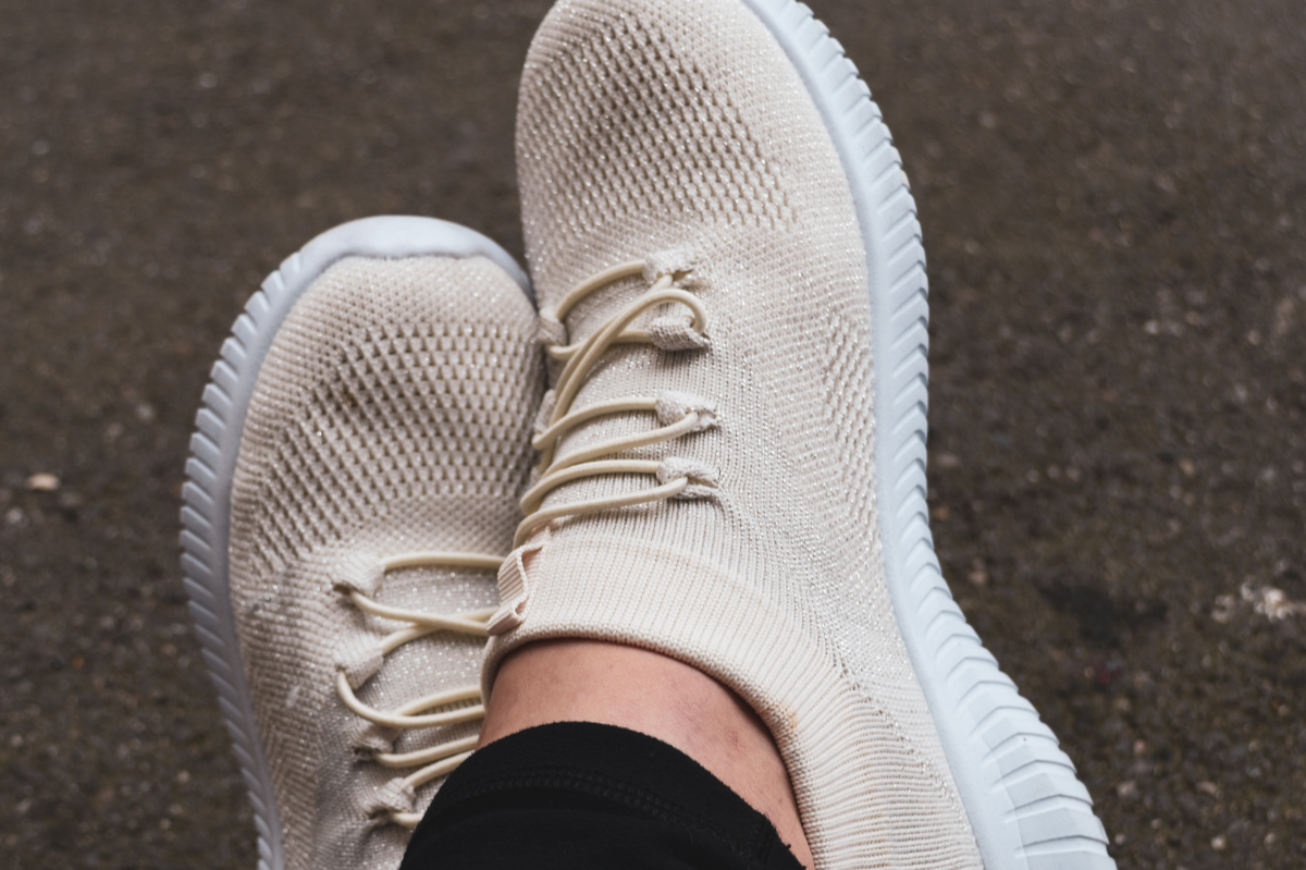 Person wearing beige athletic shoes with white soles, sitting on a textured outdoor ground.