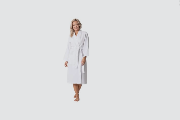 Woman in a white bathrobe standing barefoot against a plain gray background.