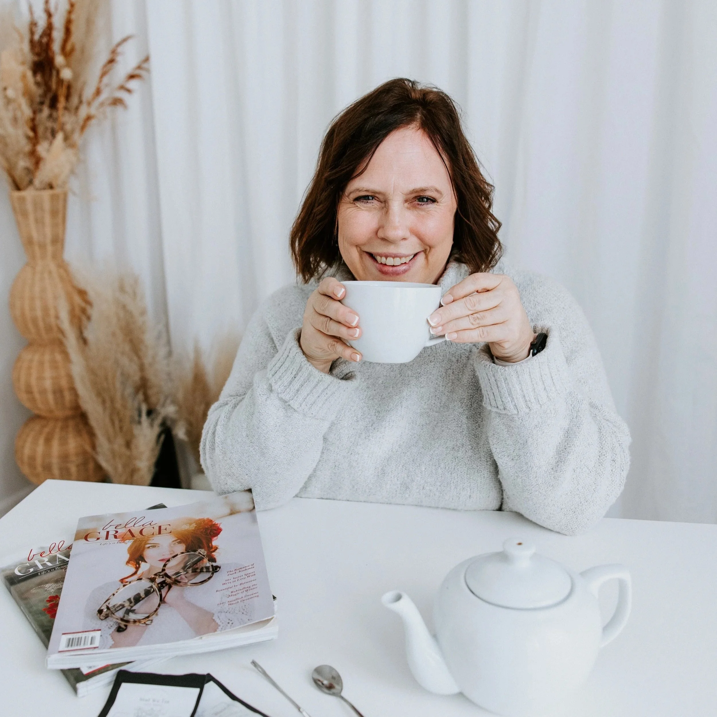 Kim Vander Poel sitting at a table with a teapot and magazines, holding a cup of tea