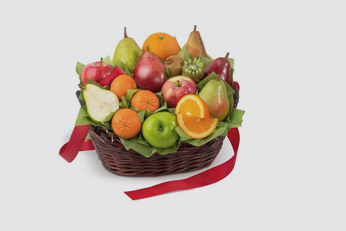 Basket of assorted fresh fruits including apples, oranges, pears, pomegranate, kiwi, and persimmons with a red ribbon on a white background.