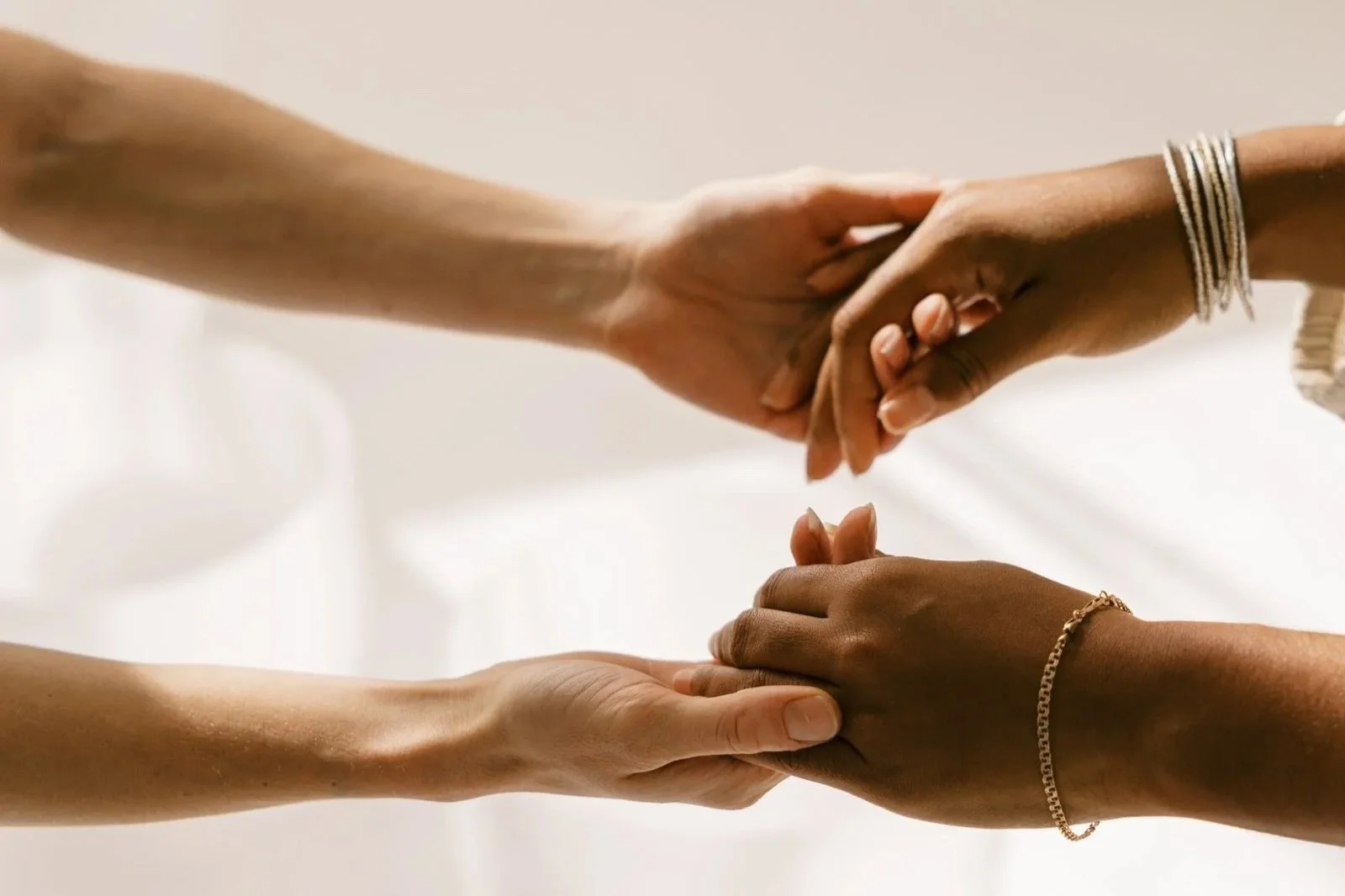 Two hands are gently holding each other, one above the other, against a soft, neutral background.