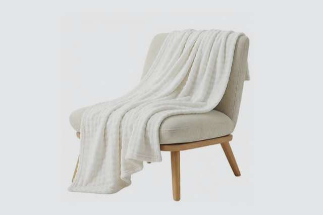 A soft cream throw blanket folded on a neutral chair, a comfort gift for someone in chemotherapy