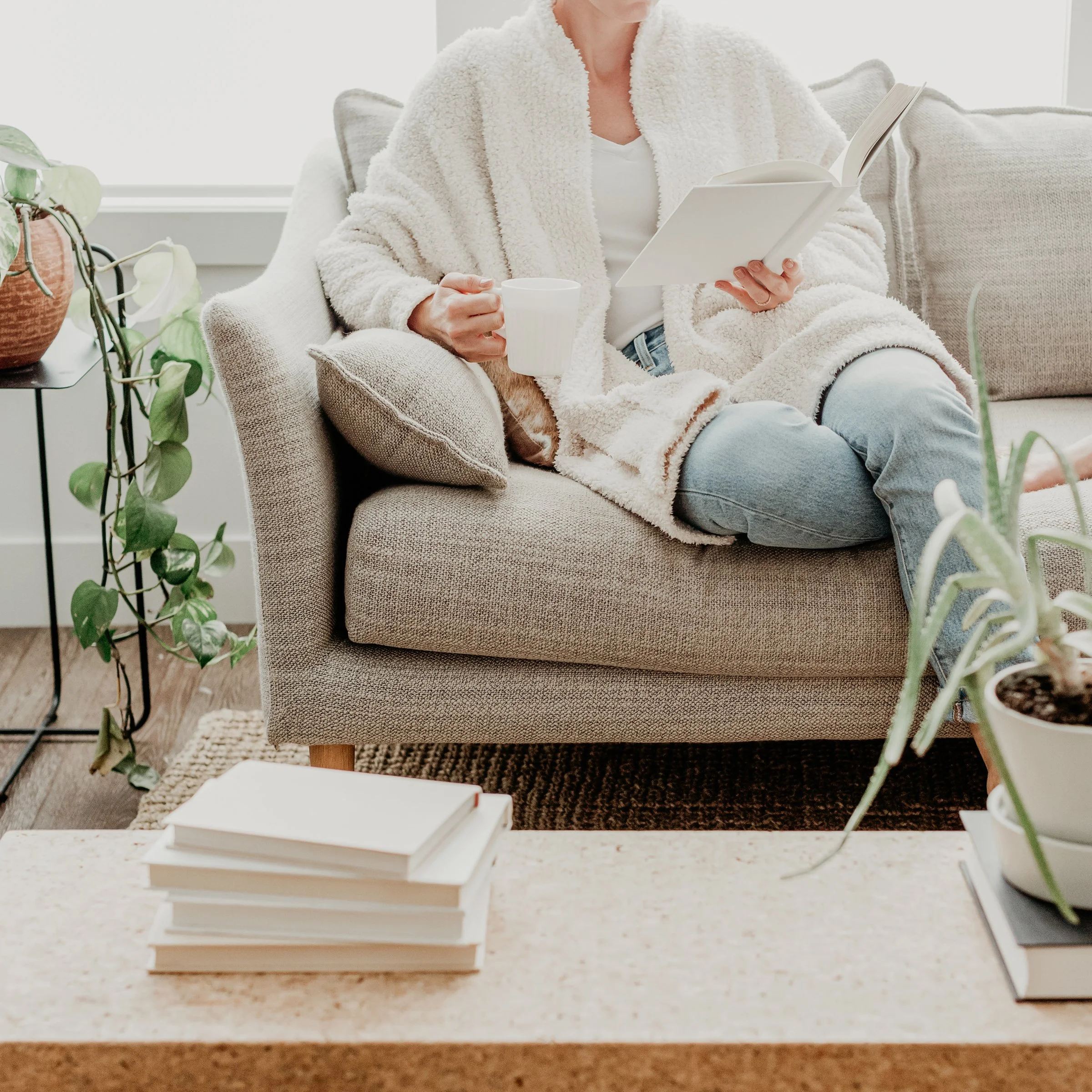 Shelf with stacked white books on a table, with a plant nearby.