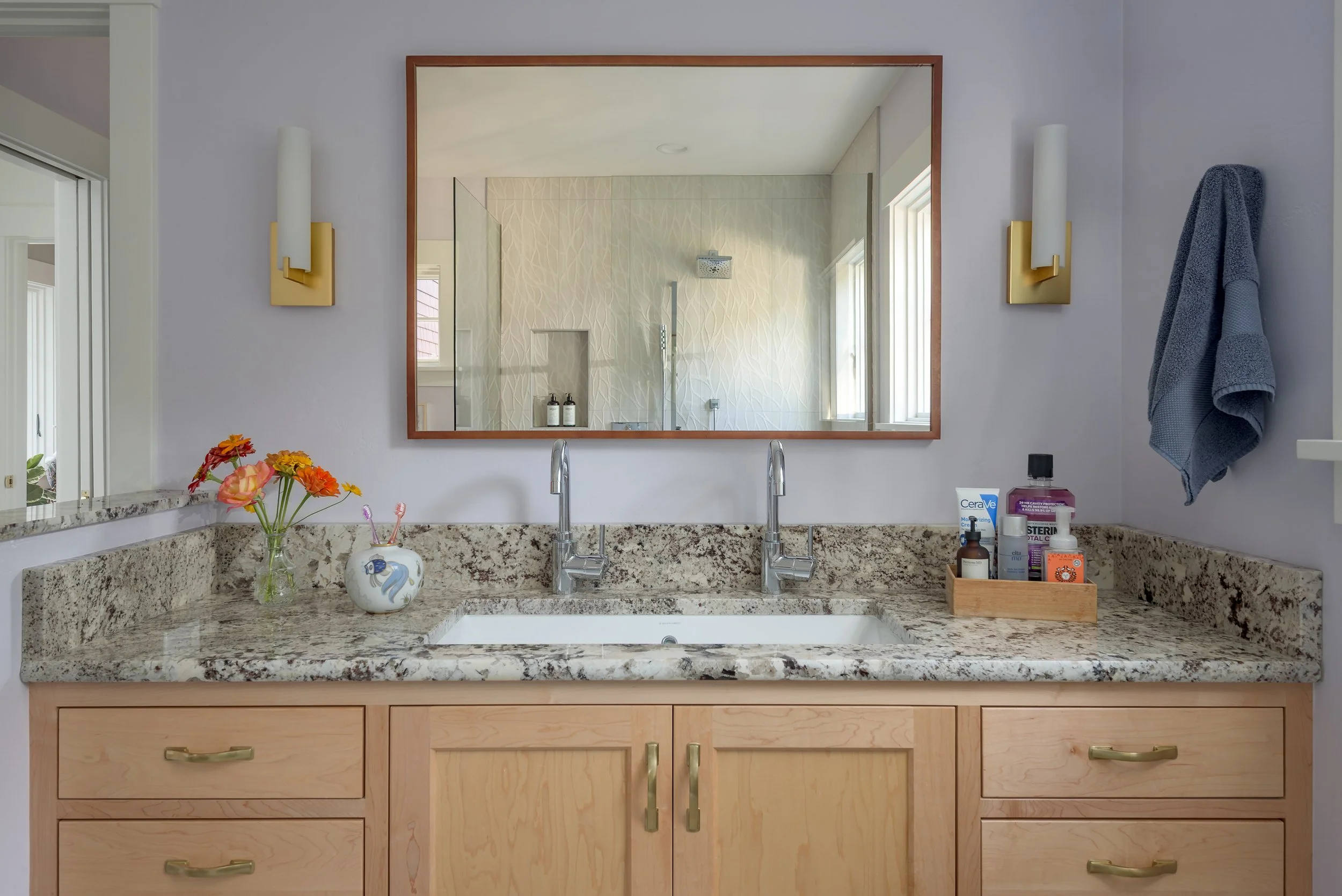 The primary bath continues the calming theme with real stone countertop, natural wood, lavender wall color, and organic wall tile in the modern shower